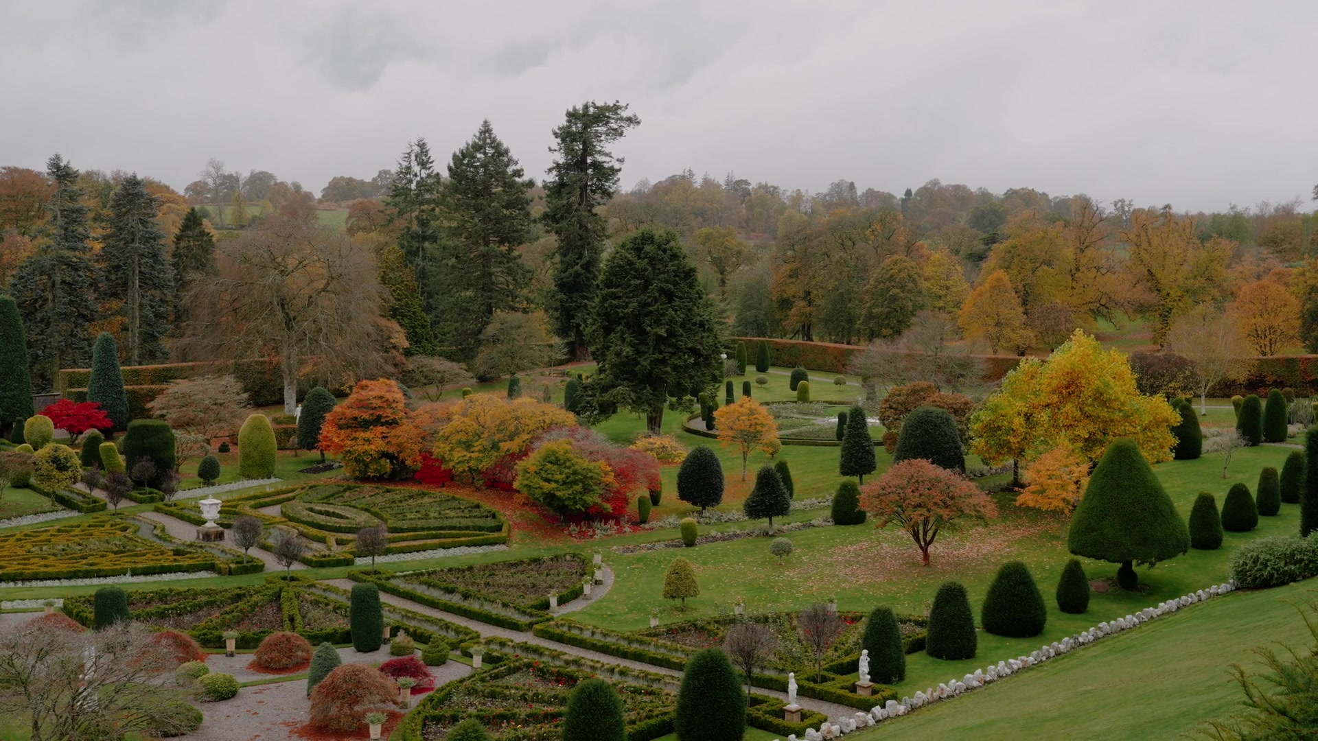 An aerial view of a formal garden shows geometric hedged beds, clipped topiary and autumn maples spread before parkland.
