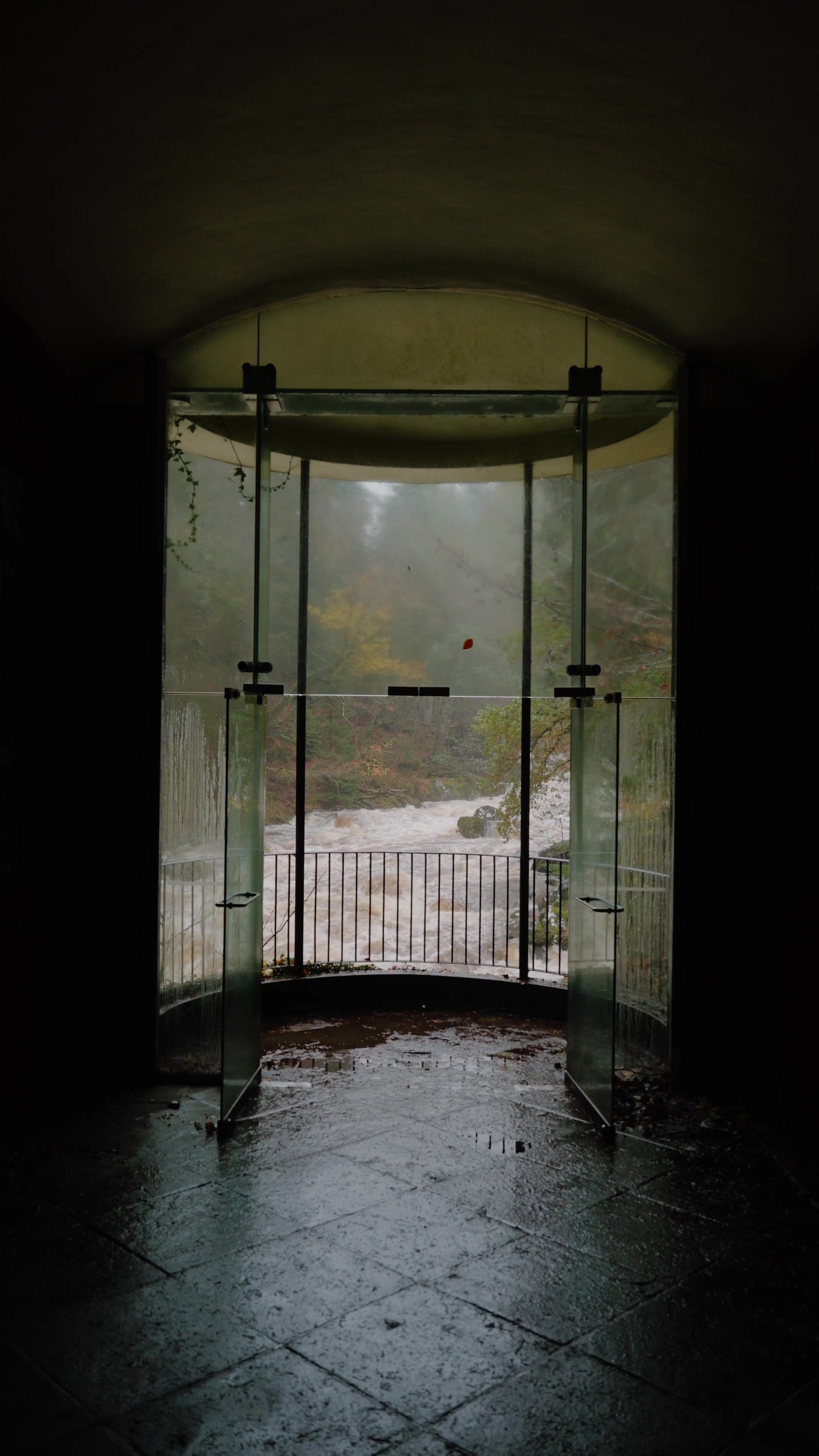 the flooded river seen through the open glass doors of Ossian's Hall's viewing pavilion, autumn trees beyond