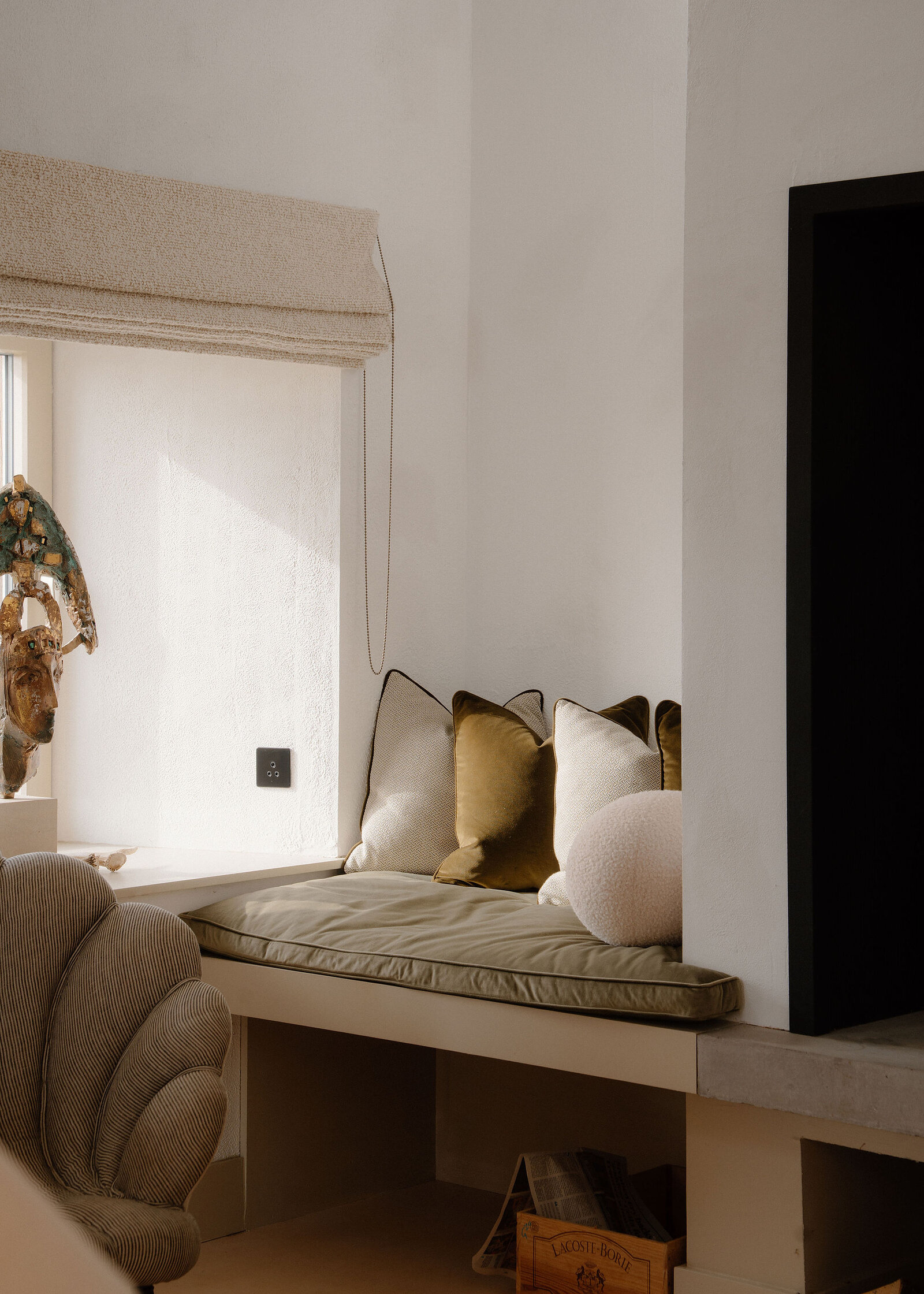 The window seat with olive and cream cushions under a linen blind, the shell armchair in front.