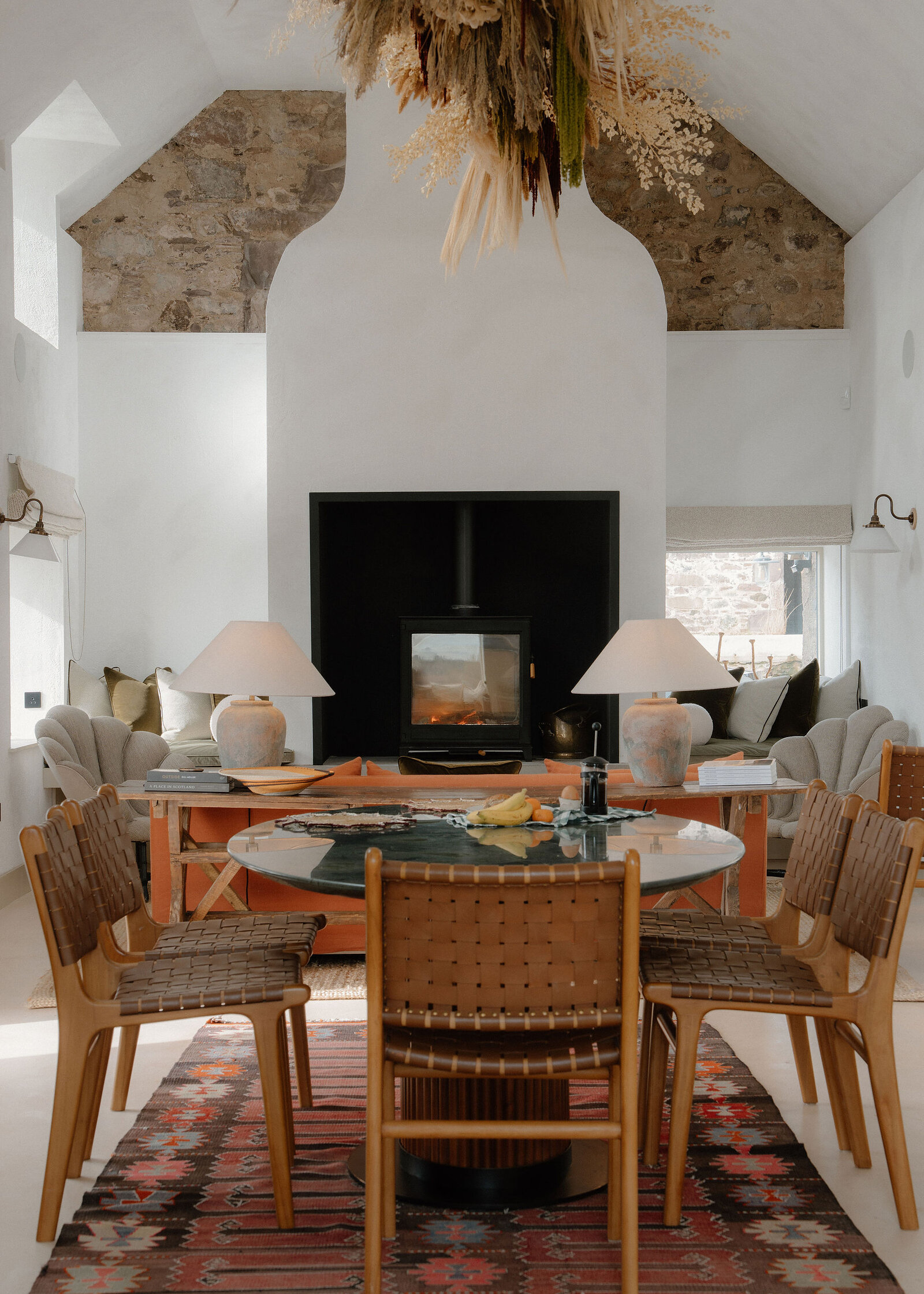 The round table and woven leather chairs on a kilim rug, the stove and sofa at the far end.