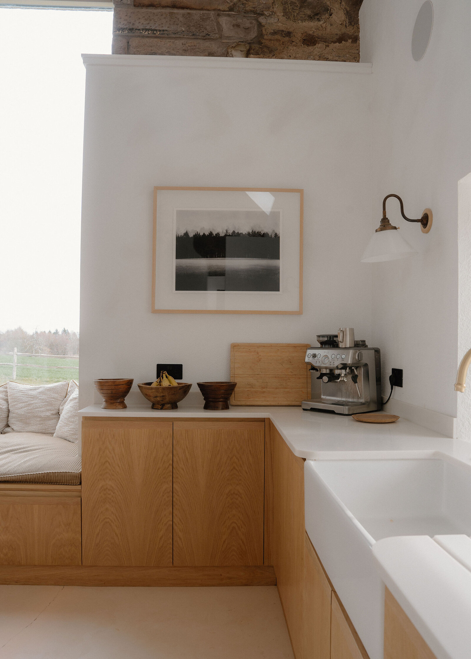 The oak kitchen with a Belfast sink and a window seat, a coffee machine and a framed photograph on the wall.