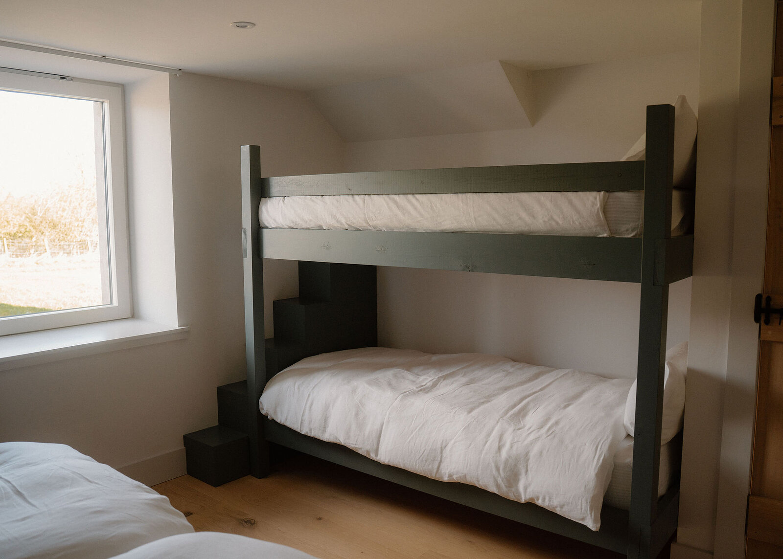 A landscape view of the upstairs room: the green double bunk, a window of fields and the end of a twin bed.