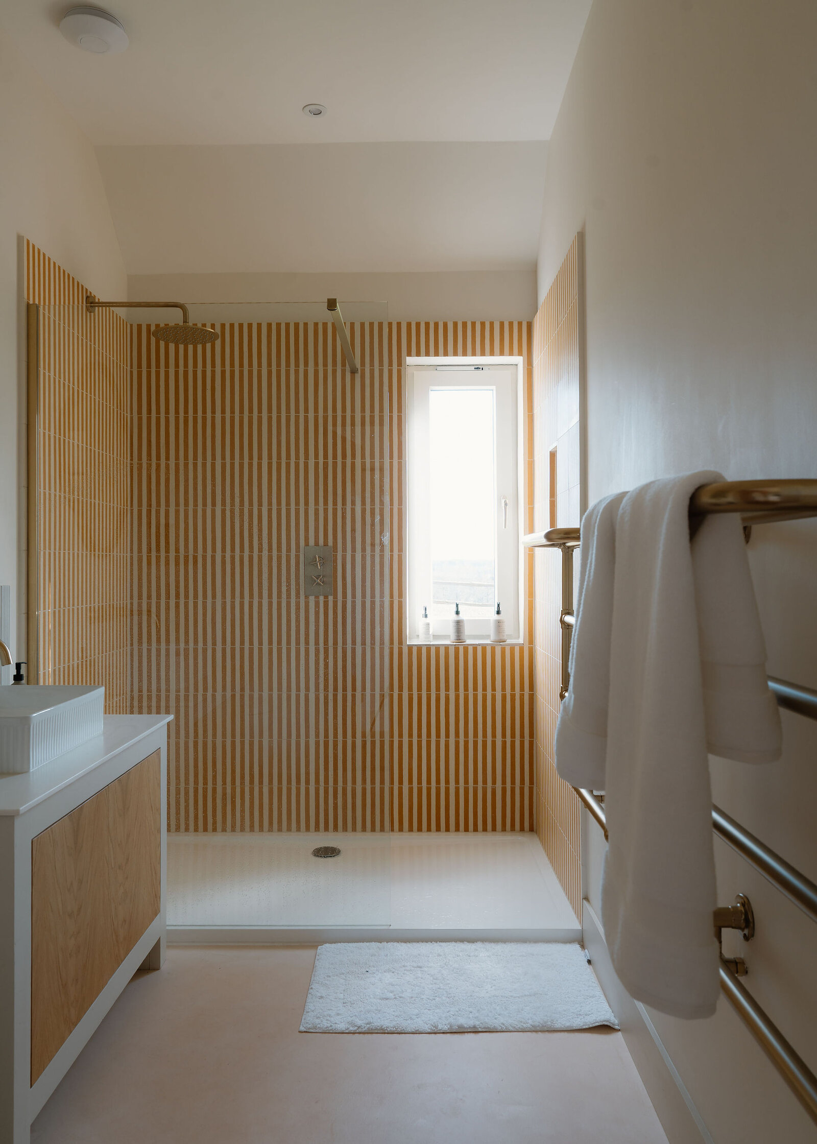 The shower room: a walk-in shower tiled in ochre stripes, an oak vanity and a heated towel rail.