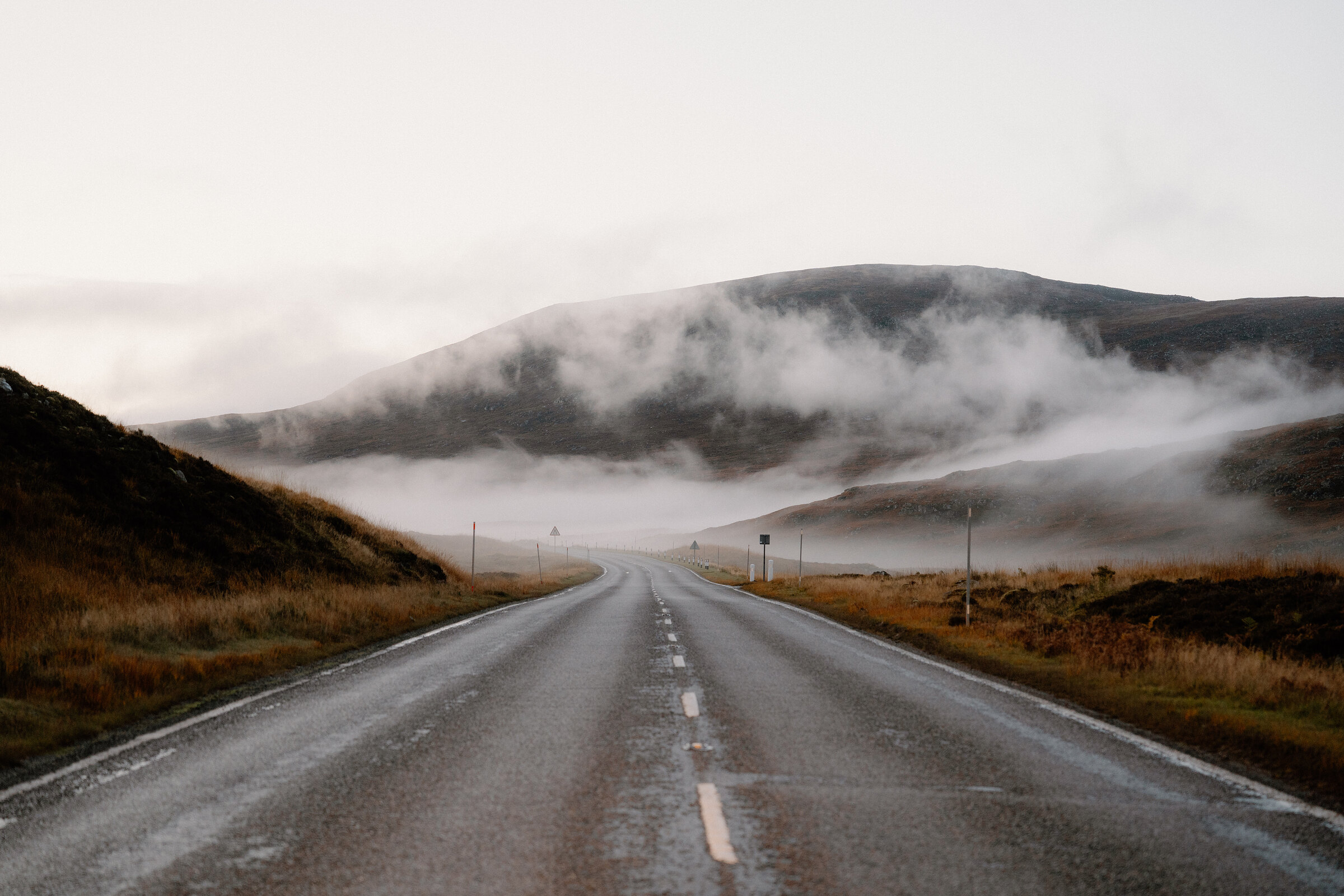 A road runs beneath mist-covered hills flanked by autumn moorland in Ross and Cromarty.