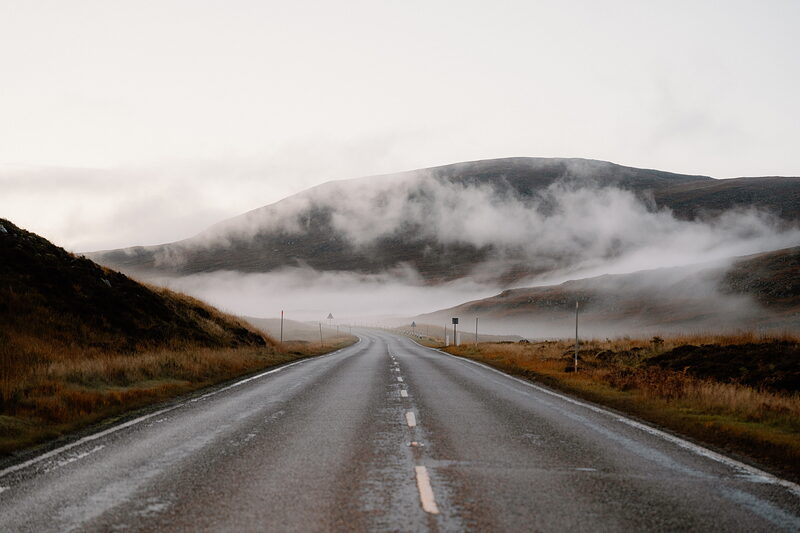 A road runs beneath mist-covered hills flanked by autumn moorland in Ross and Cromarty.