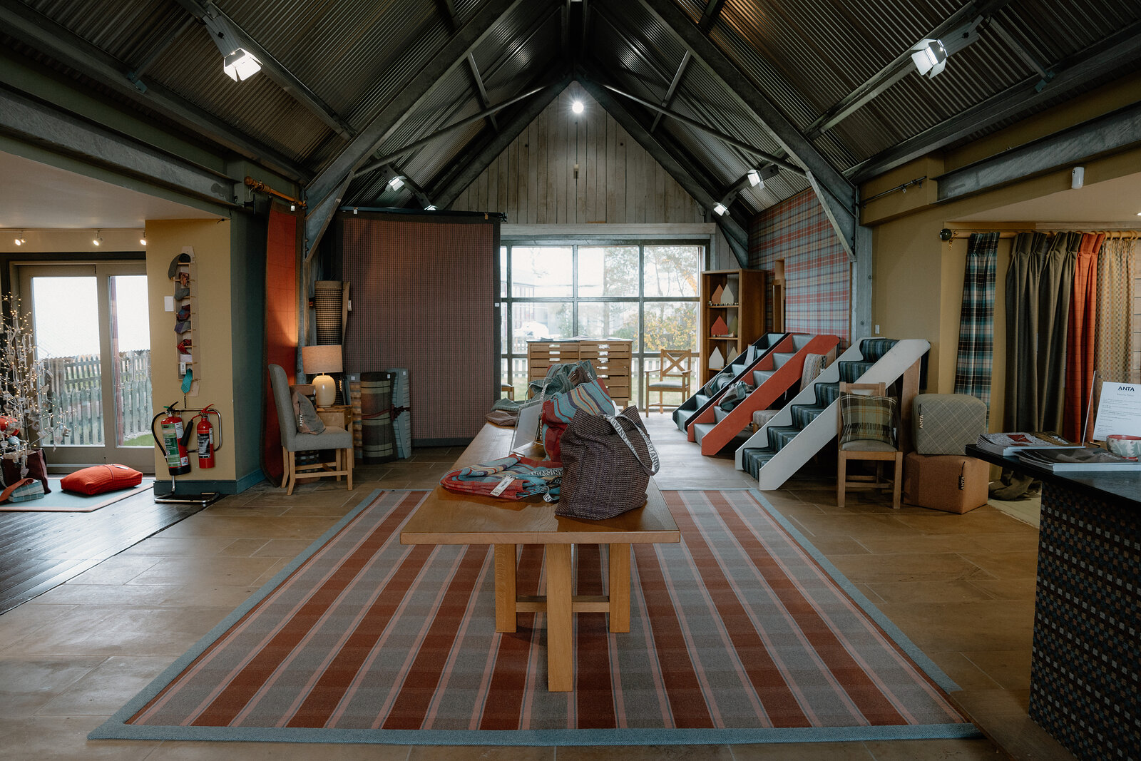 ANTA's showroom displays folded throws and cushions beneath a vaulted corrugated-metal roof.
