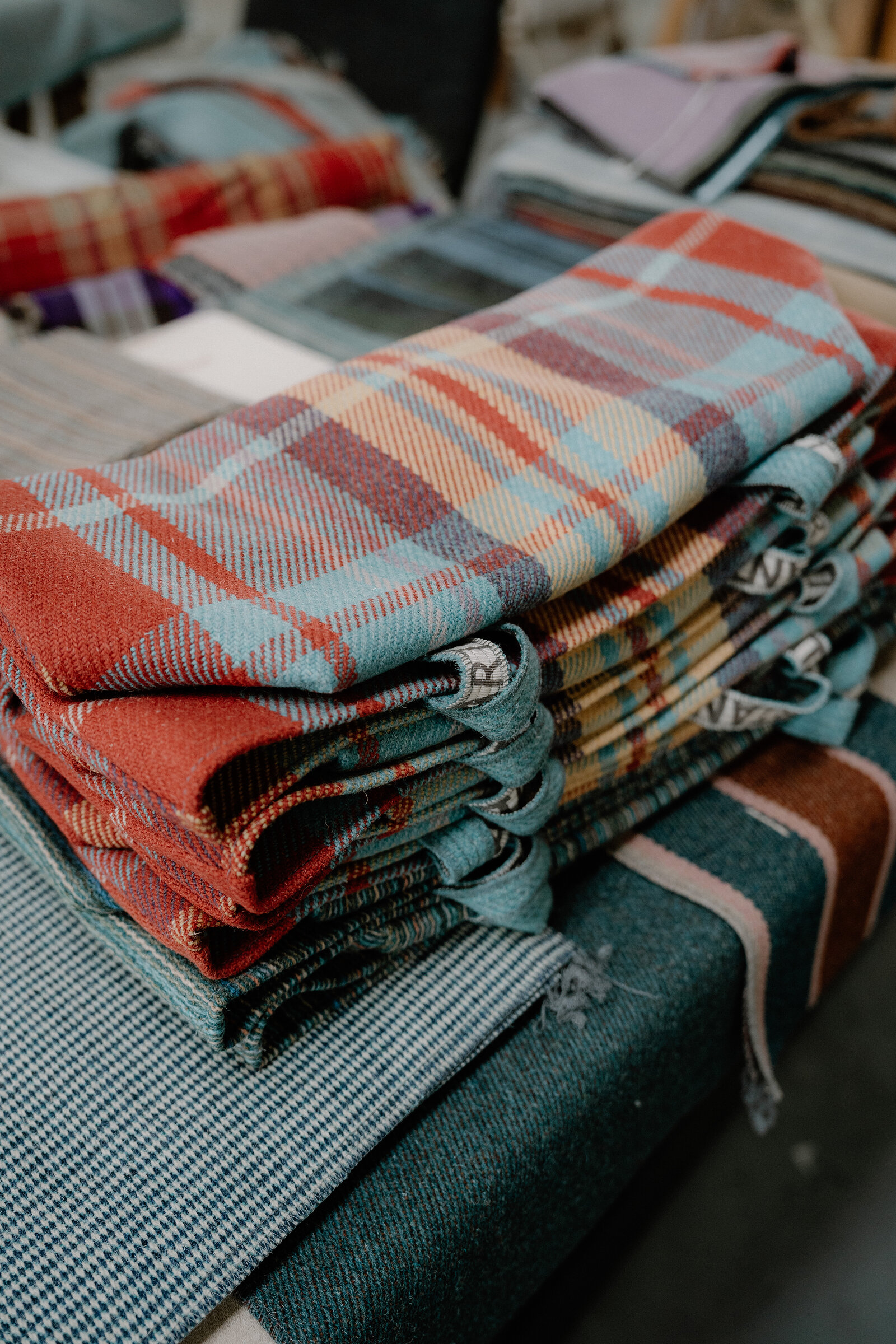 Folded tartan and check throws in blue, red and grey are stacked on wooden shelving at ANTA.