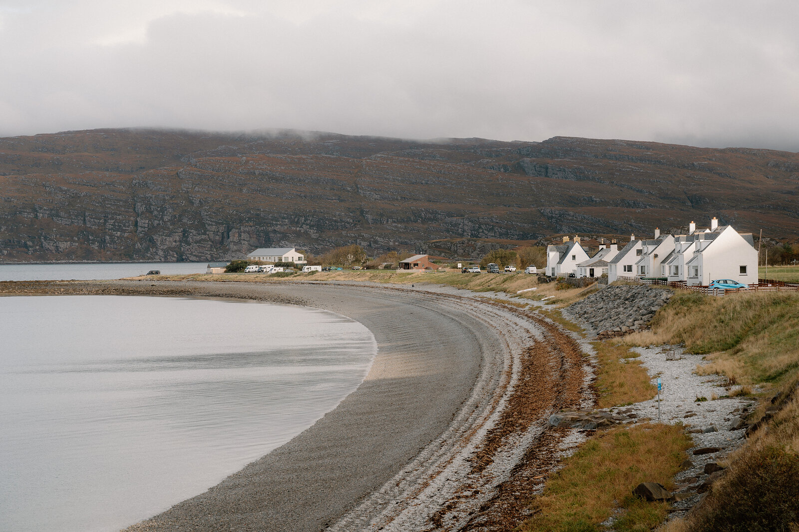 White cottages overlook a curving shingle beach beneath misty hills in Ross and Cromarty.