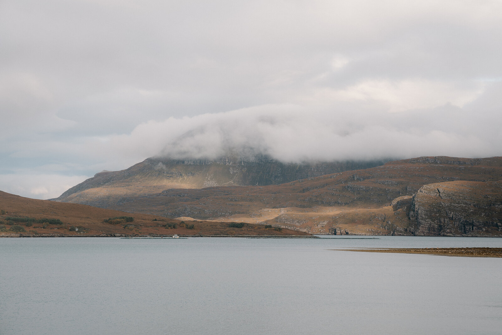 Low cloud clings to a cliff-edged hill above a calm sea loch in Ross and Cromarty.