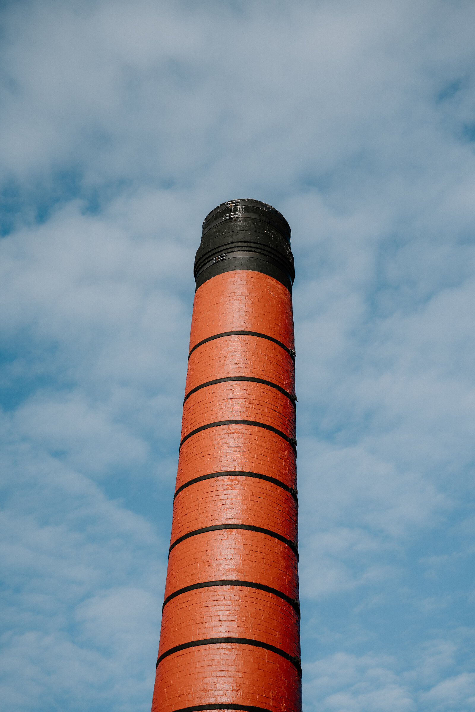 A banded red-brick chimney rises against a partly cloudy sky at Balblair distillery.