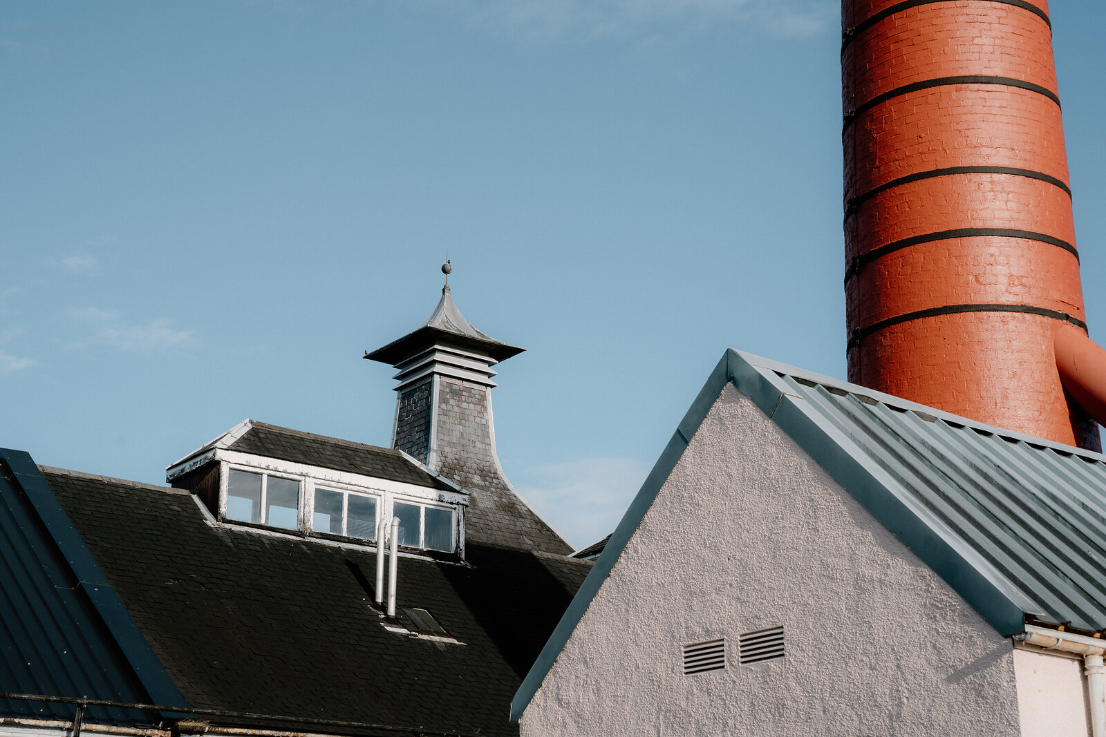 A red-brick chimney rises beside slate and metal roofs at Balblair distillery.
