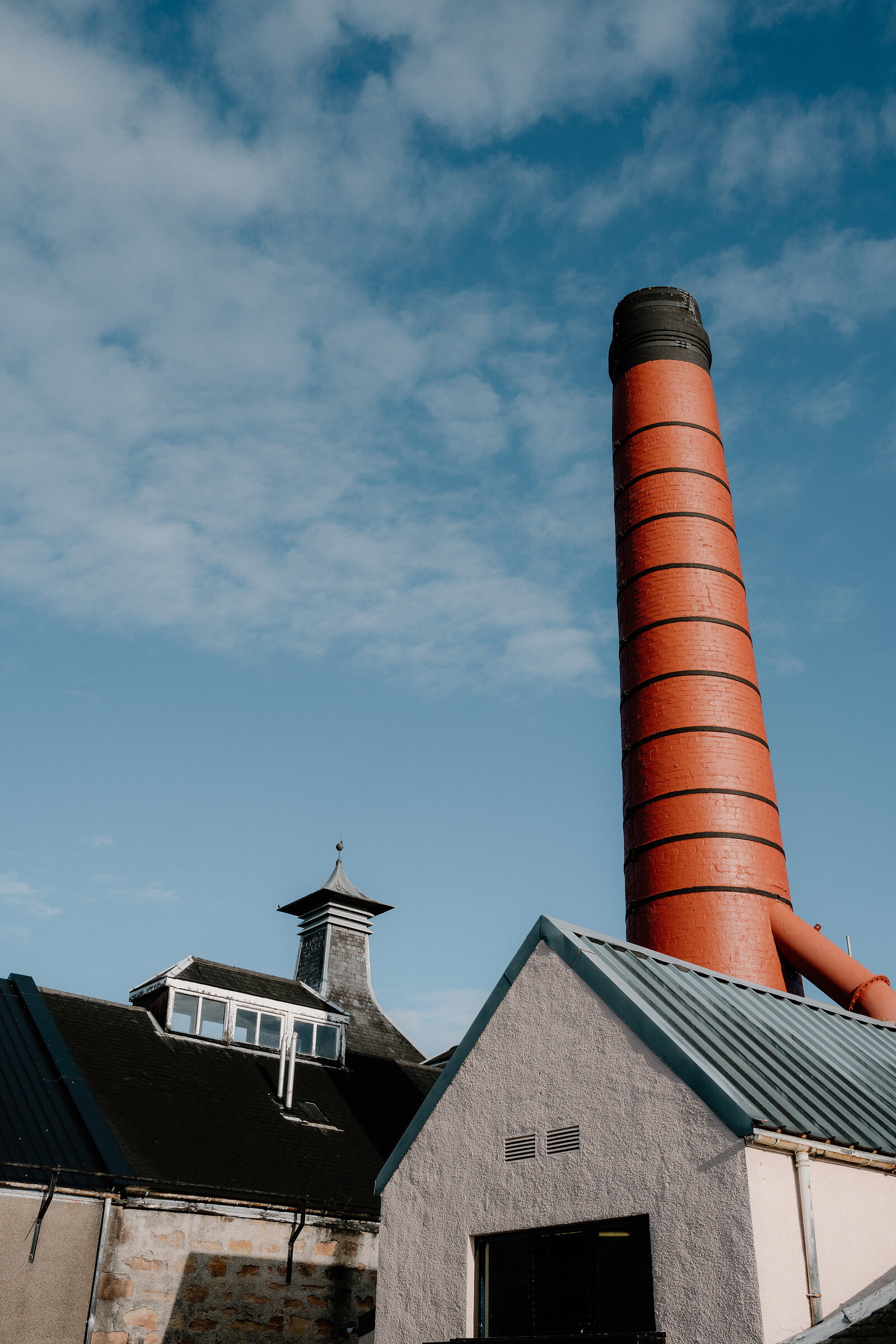 A tall banded red-brick chimney towers over Balblair distillery's gabled buildings.