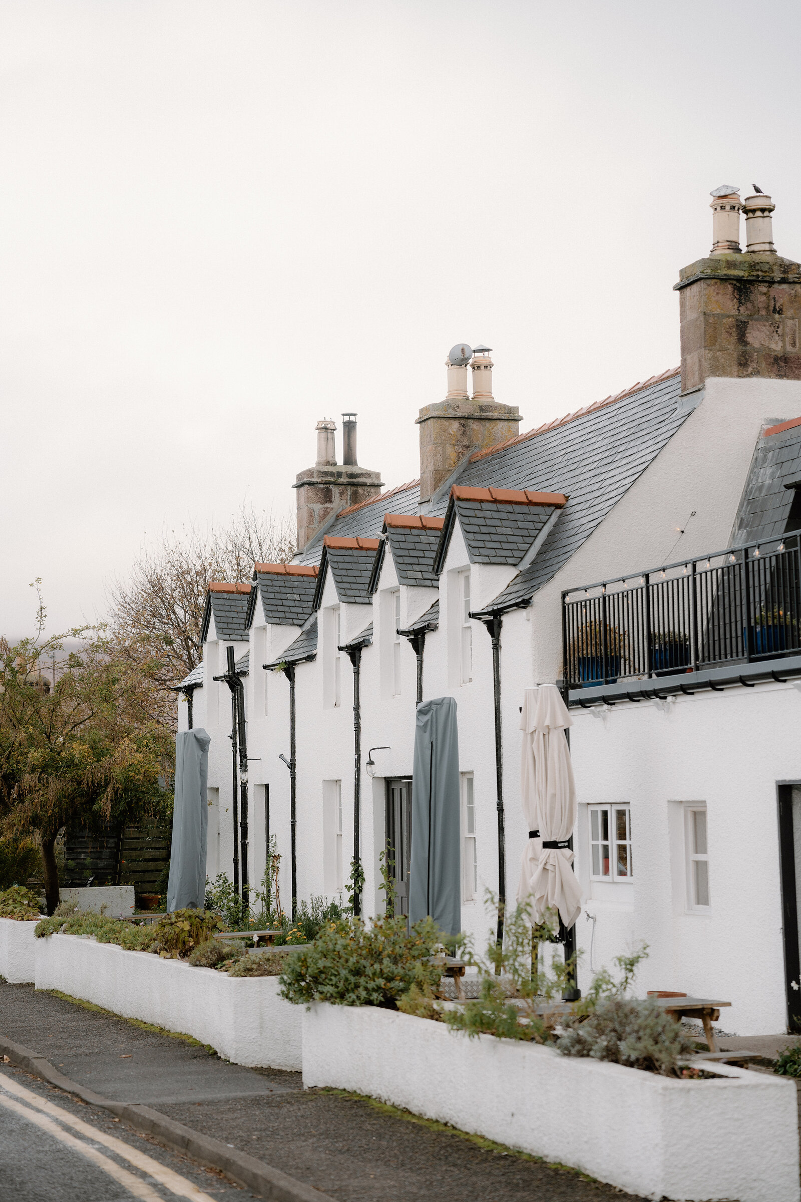A row of white-harled cottages with slate roofs and a rooftop balcony lines a street in Ross and Cromarty.