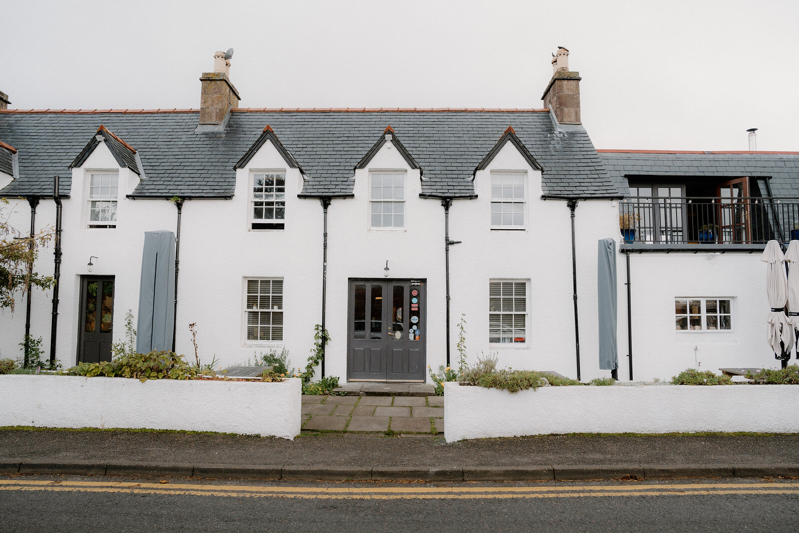A white-harled cottage with dormer windows and a walled garden sits on a Ross and Cromarty street corner.