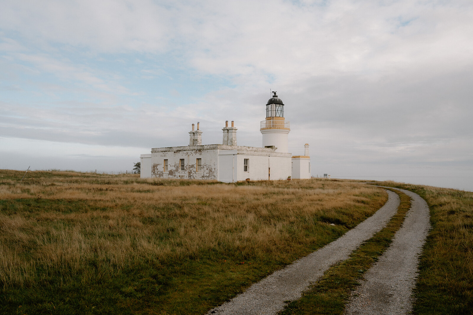 Chanonry Point Lighthouse and its keeper's cottages sit among rough grass beside a winding track in Ross and Cromarty.