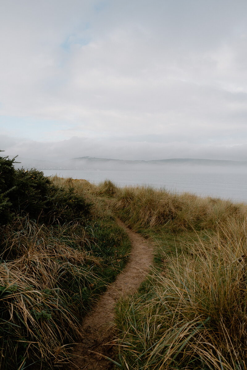 A sandy path winds through dune grass toward a misty sea view in Ross and Cromarty.