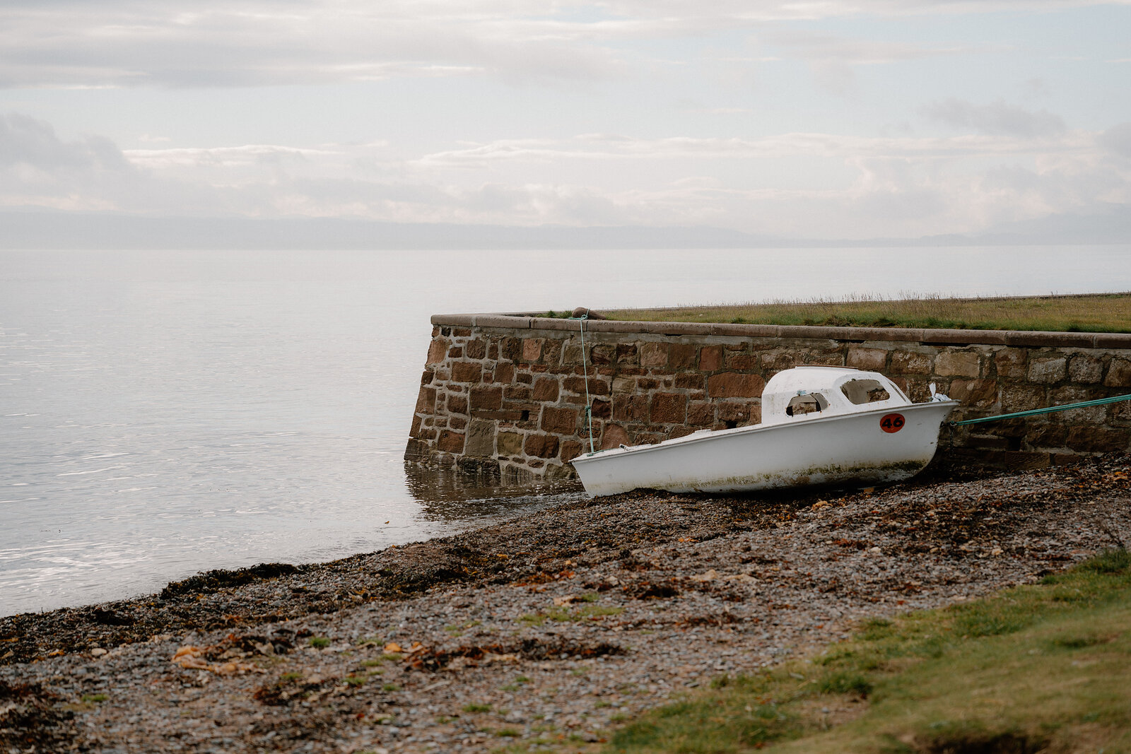 A small white boat rests on the shingle beside a stone harbour wall in Ross and Cromarty.