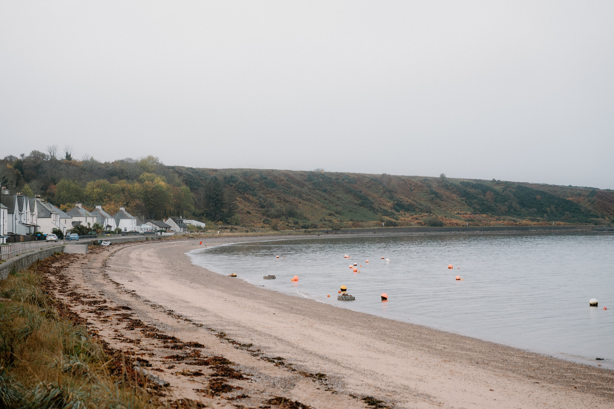 The beach curving round the bay at Cromarty, white houses along the shore and boats moored off.