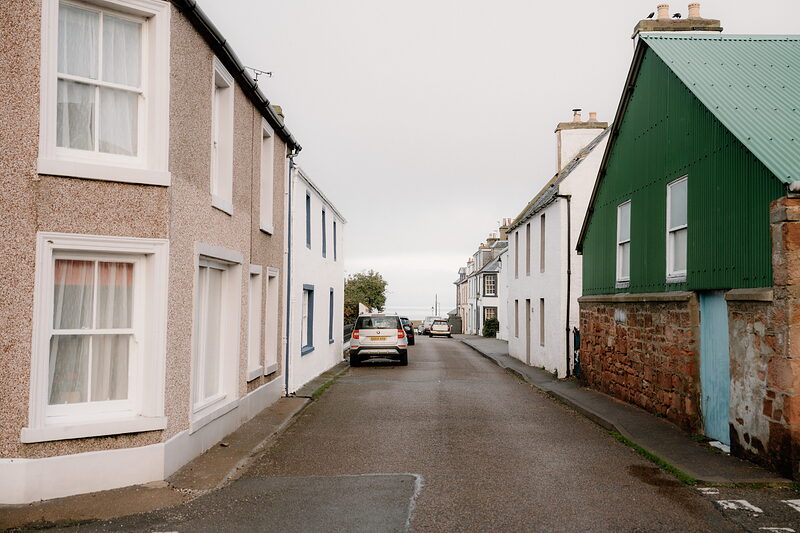 A street of white and green-roofed houses curves past a parked car in Cromarty.