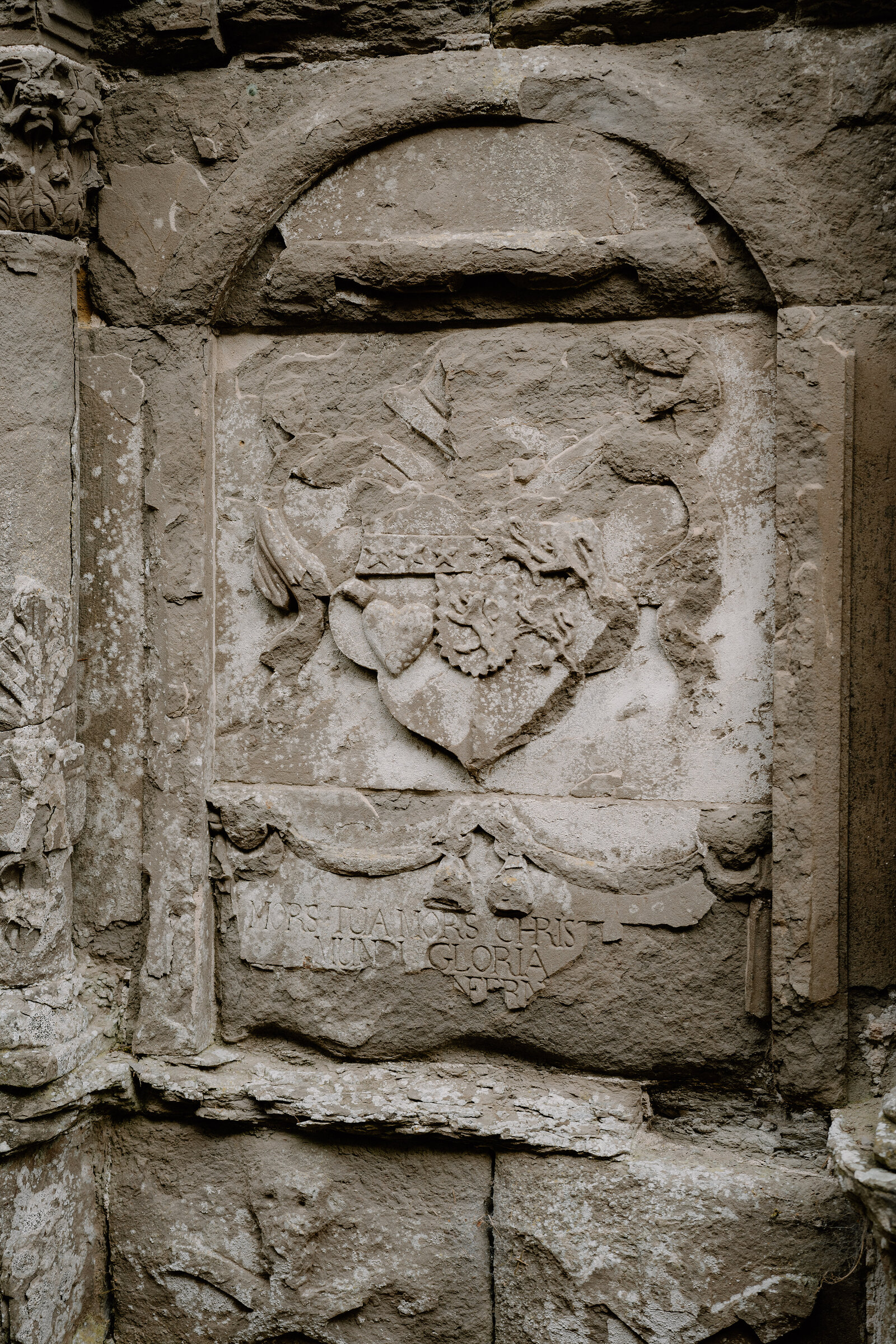 A weathered heraldic carving with a Latin inscription is set into the wall of a ruined Ross and Cromarty church.