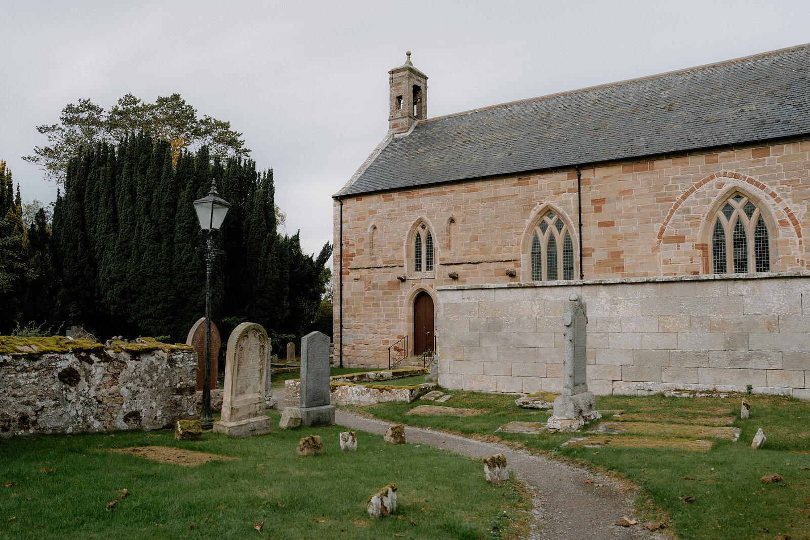 A weathered stone cross memorial stands among gravestones in a Ross and Cromarty churchyard in autumn.