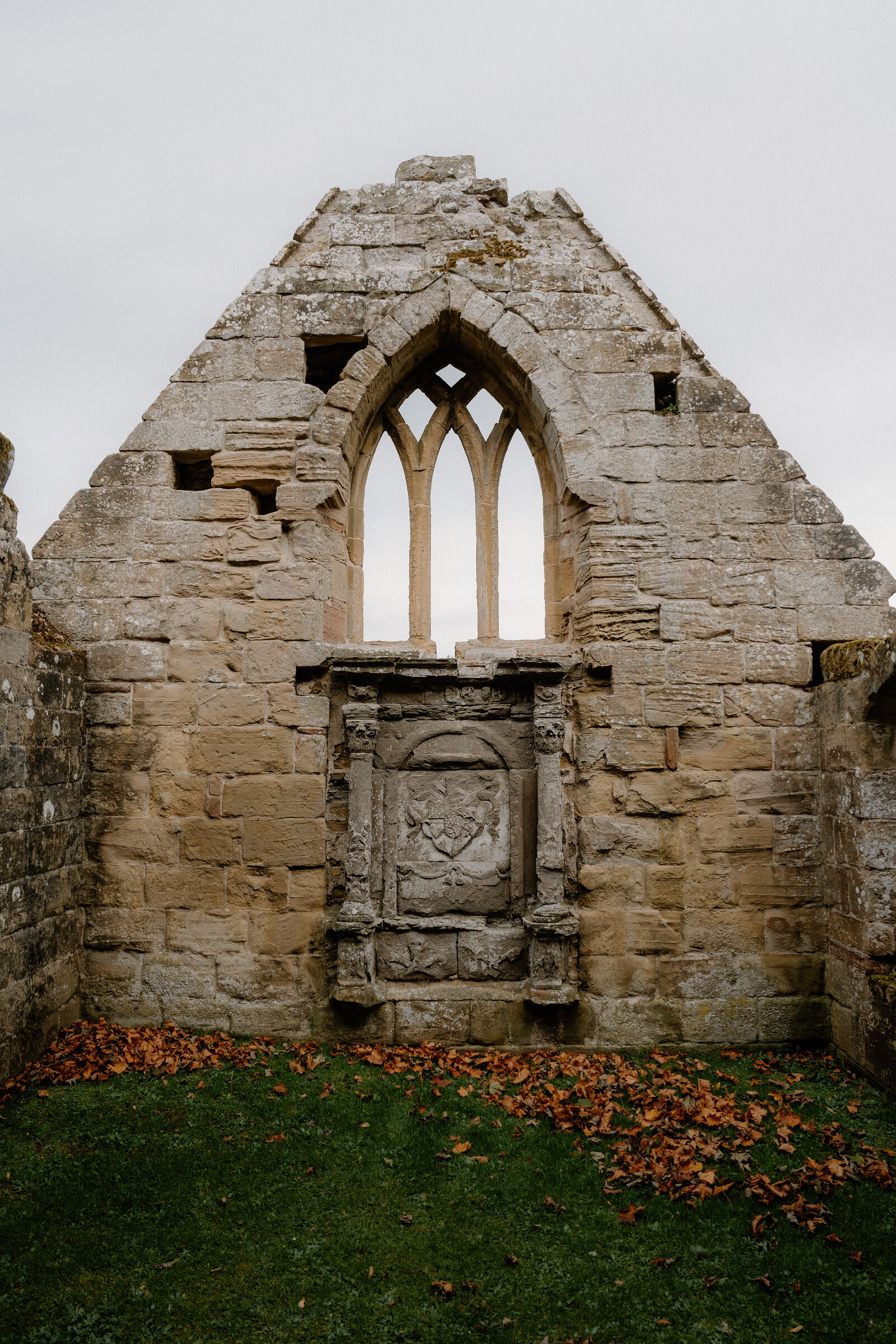 A traceried gothic window and a carved heraldic panel survive in the gable of a ruined Ross and Cromarty church.