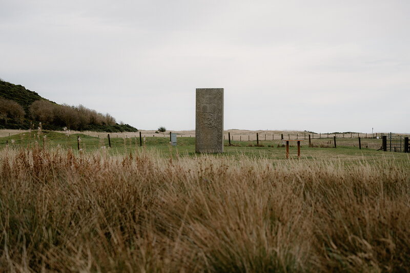 A carved standing stone stands in open grassland with dune grass beyond on the Ross and Cromarty coast.