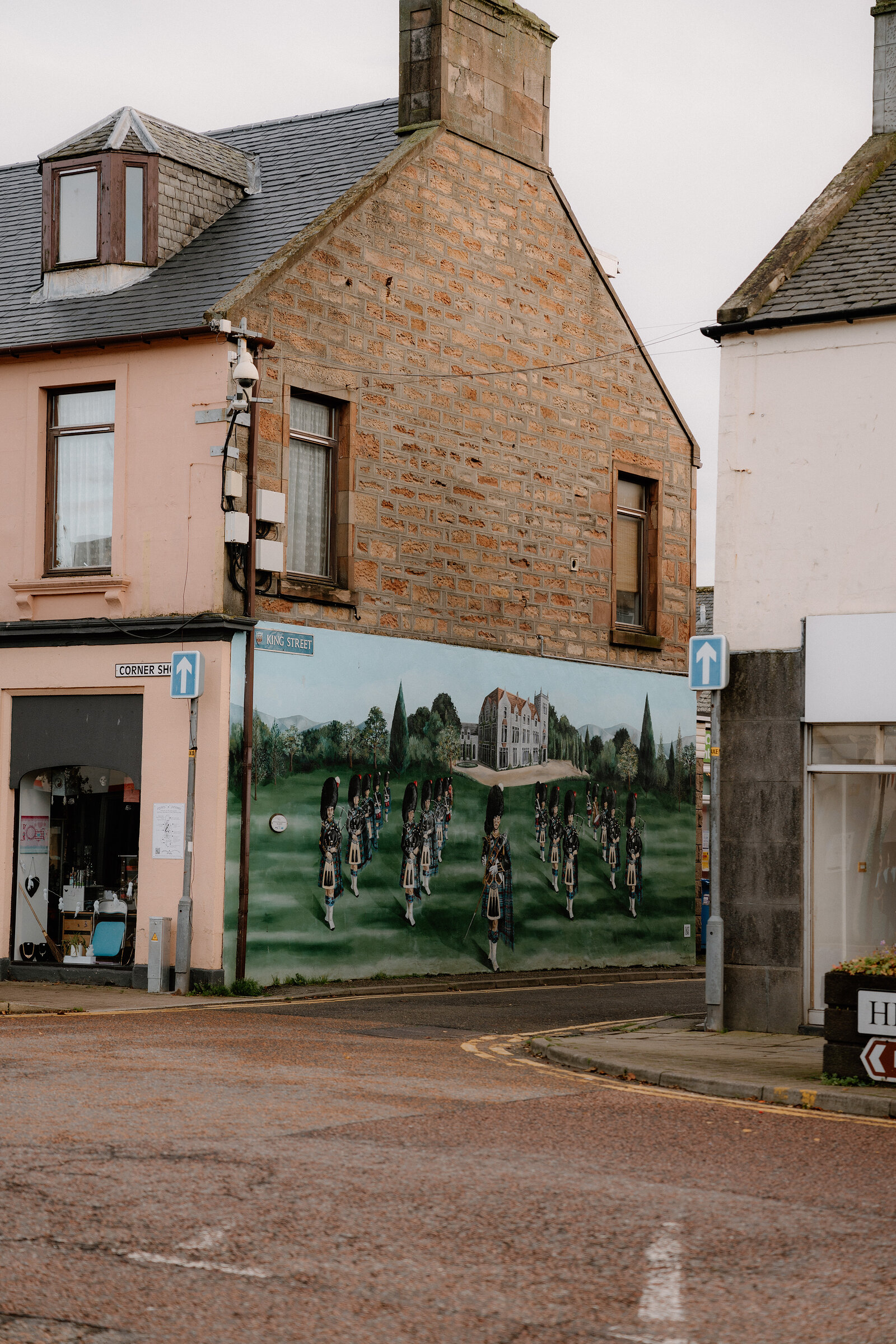 The Invergordon Highland Gathering mural spans a gable end above a pink corner shop, Ross and Cromarty.