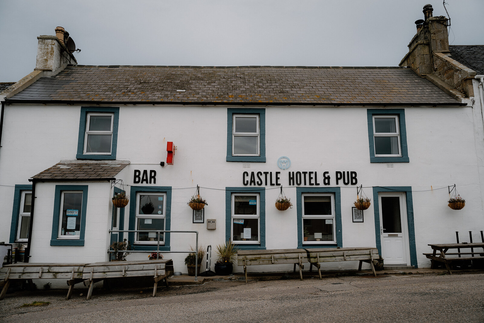 The Castle Hotel & Pub's sign and bar entrance sit beneath teal-trimmed windows and picnic benches.