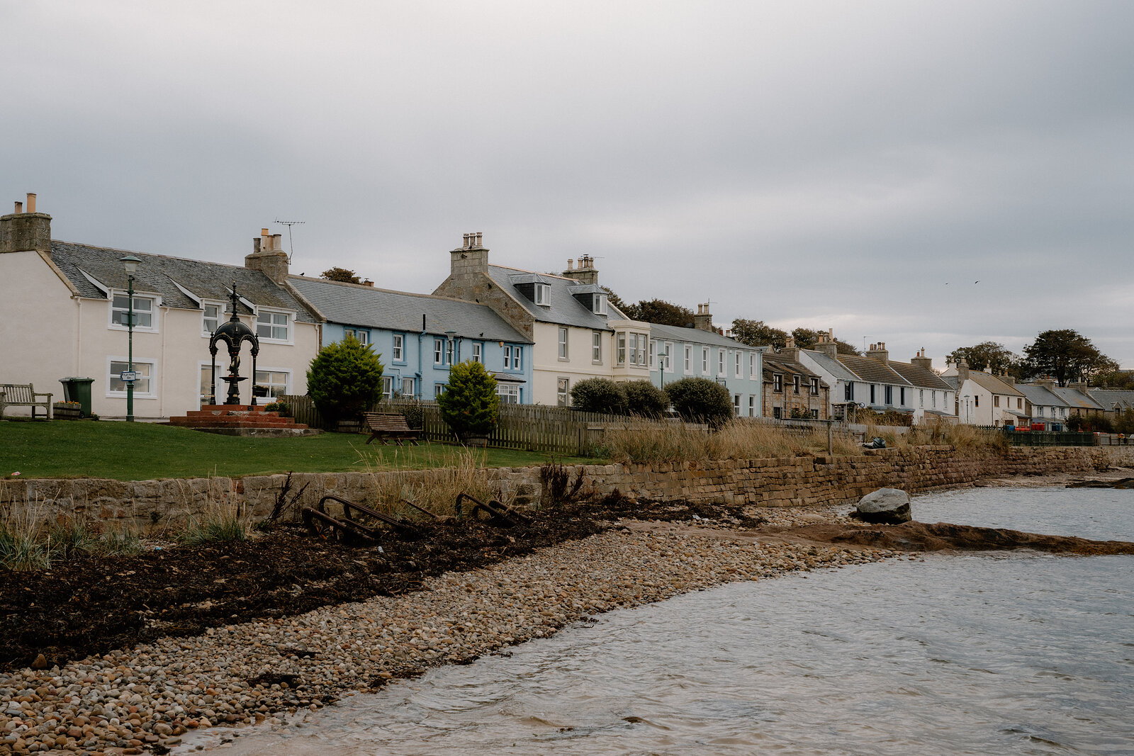 A row of pastel-painted houses fronts a pebble shore in a Ross and Cromarty coastal village.