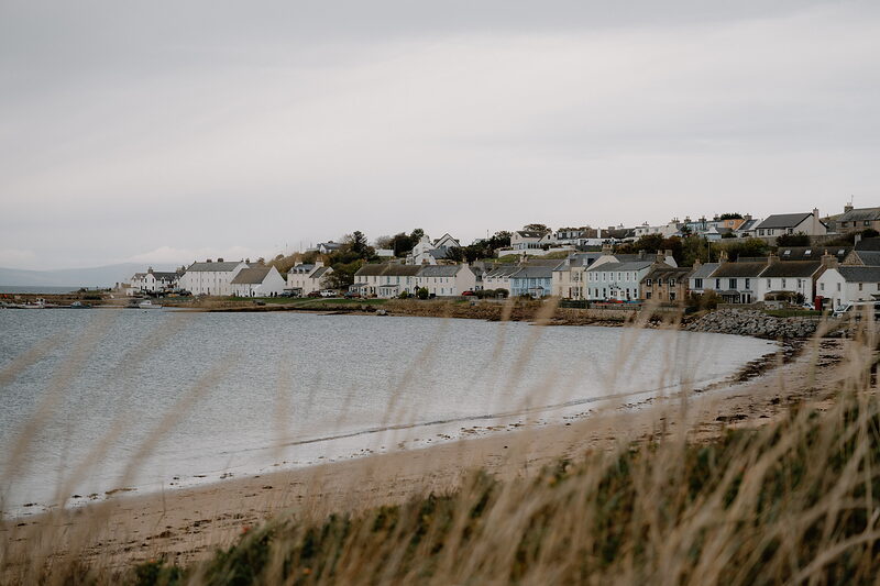 A Ross and Cromarty coastal village curves around a sandy bay, marram grass framing the view.
