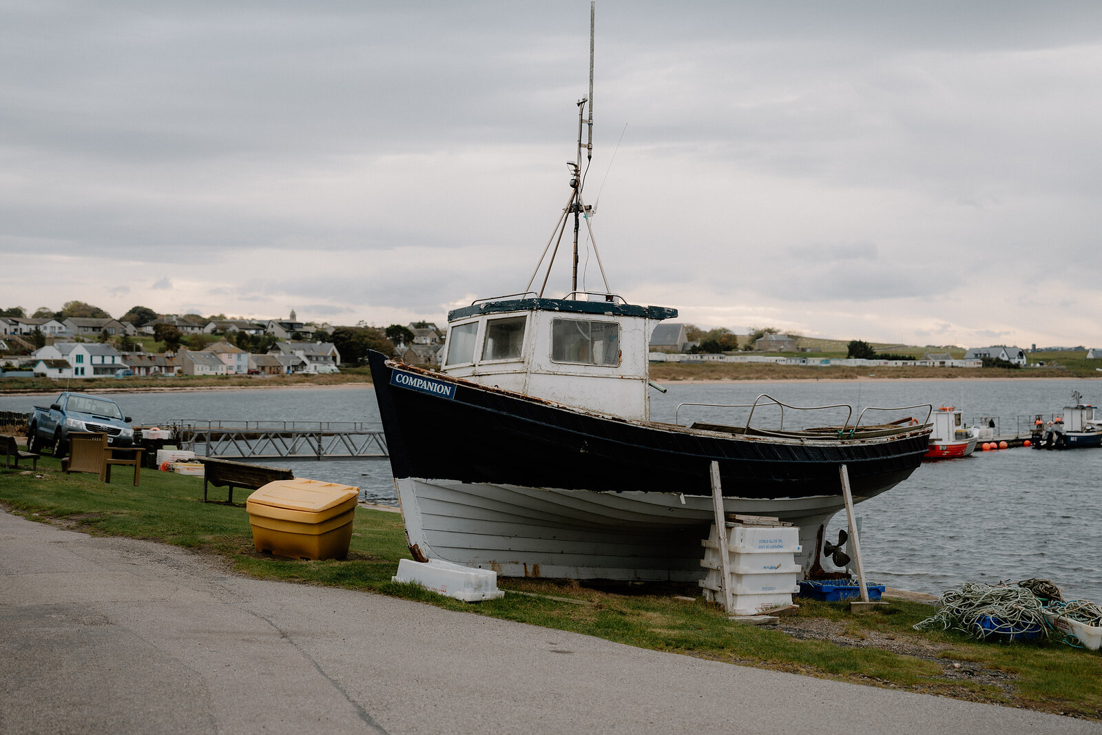 A weathered fishing boat rests on a slipway beside a Ross and Cromarty harbour.