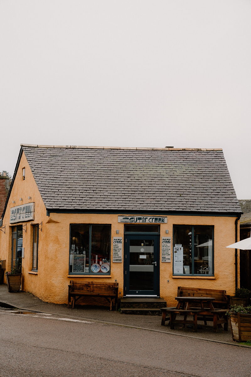 Sutor Creek's yellow shopfront sits on a quiet street corner, wooden benches set outside.