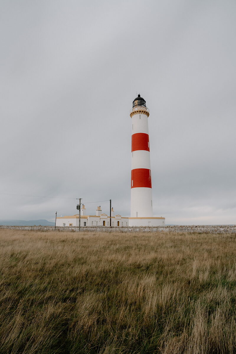 Tarbat Ness Lighthouse rises above grassland at the end of a rocky coastline in Ross and Cromarty.