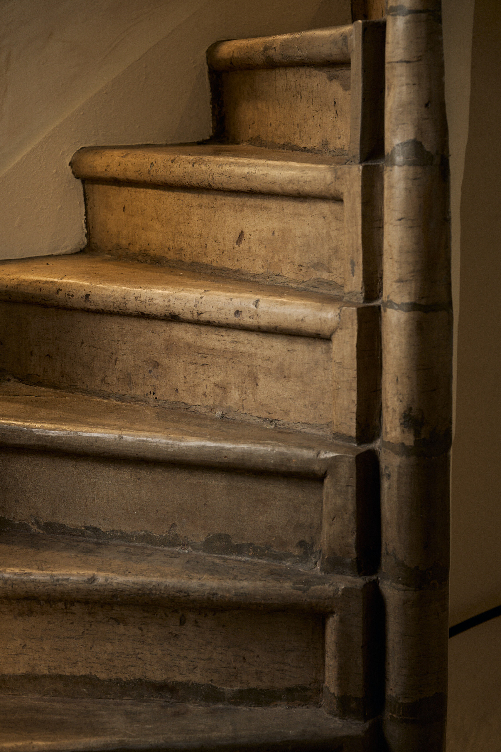 A weathered wooden spiral staircase curves upward, its worn treads and newel post lit from one side.