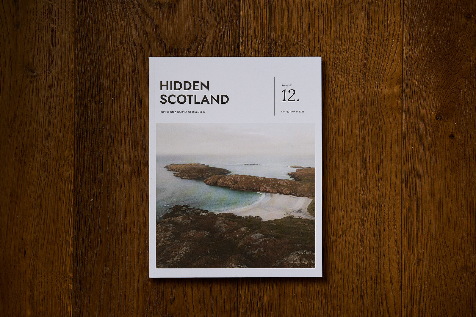 Issue 12 lying on a wooden floor, its cover a sea cliff and a sandy bay