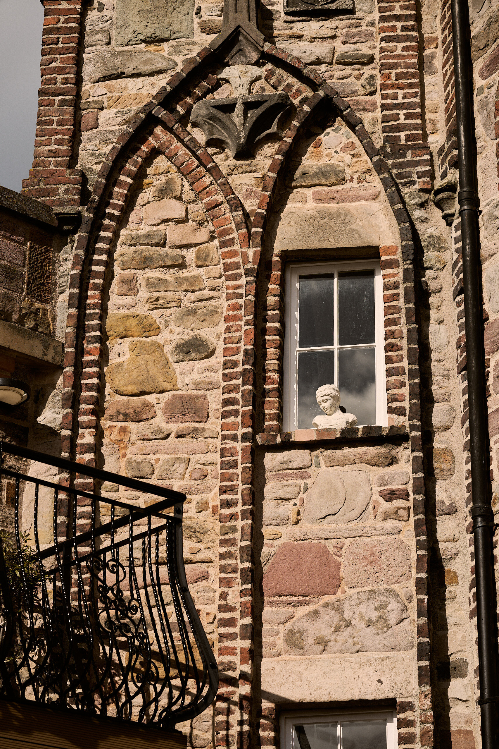 Gothic-arched stone and brick window with a small bust set inside, a wrought-iron balcony below