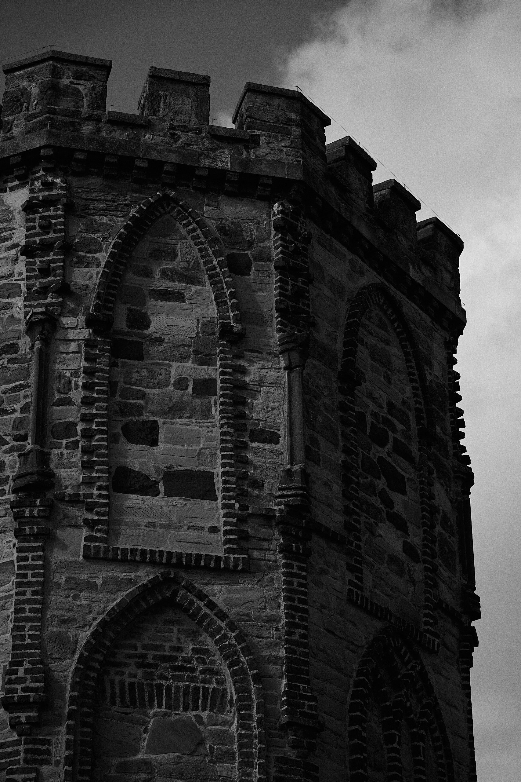 Castellated stone tower corner with gothic-arched windows, in black and white