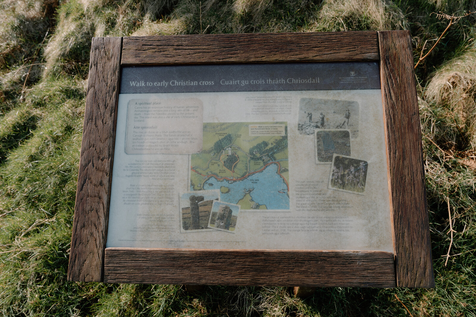 A wooden interpretive sign describes a 'Walk to early Christian cross' in English and Gaelic beside a map.