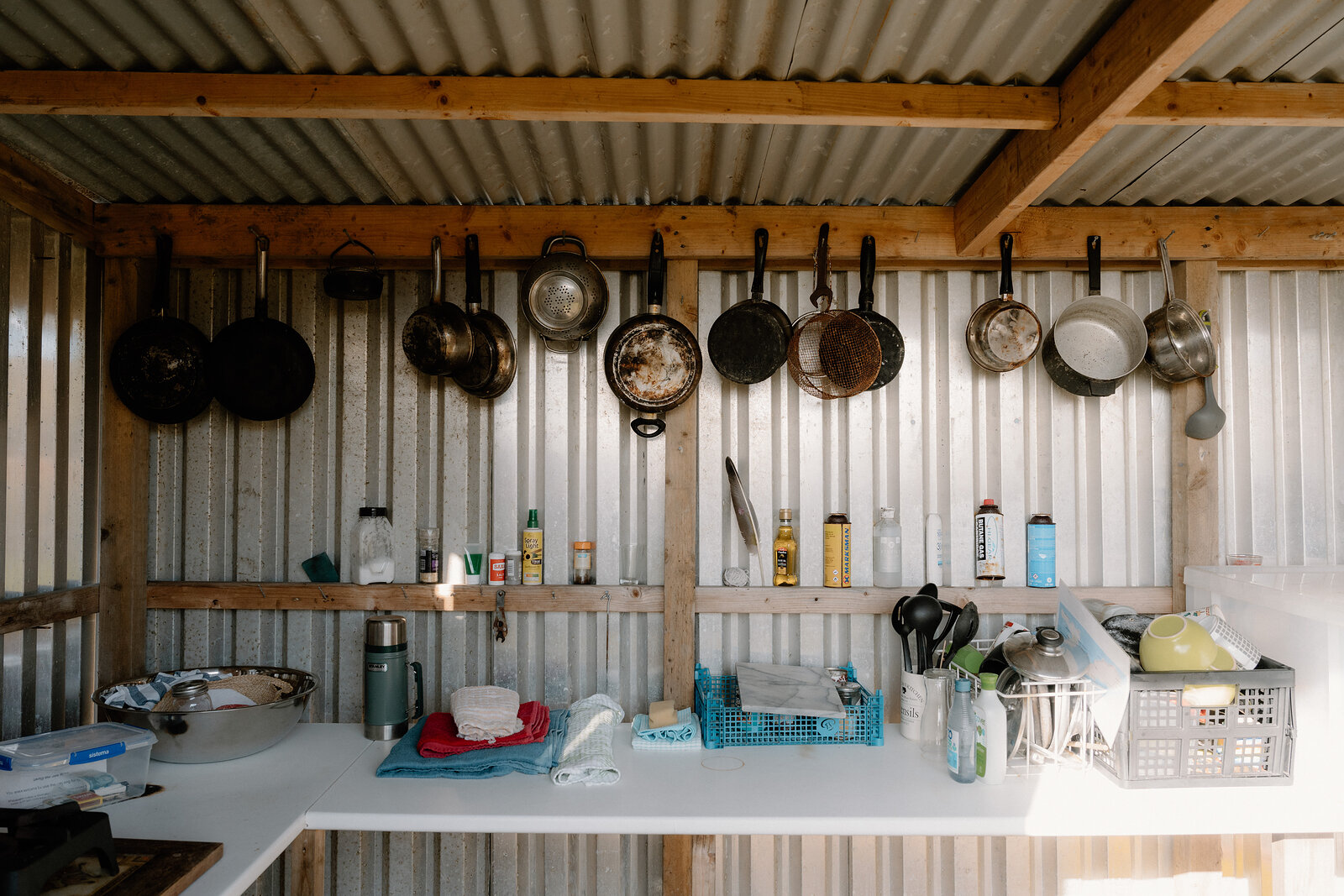 A row of pans hangs above a shelf of condiments inside a camping kitchen shed on the Isle of Canna.