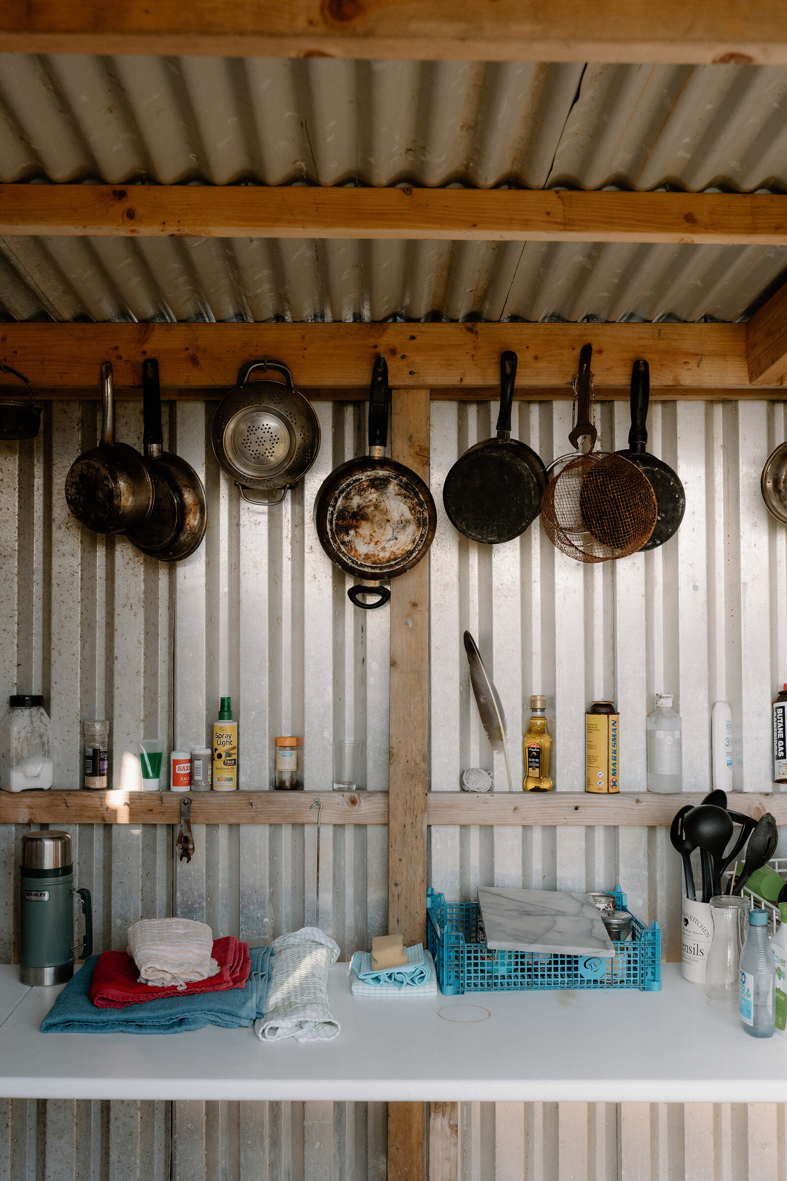 Hanging pans and a blue crate sit above a worktop inside a corrugated-iron kitchen shed on the Isle of Canna.