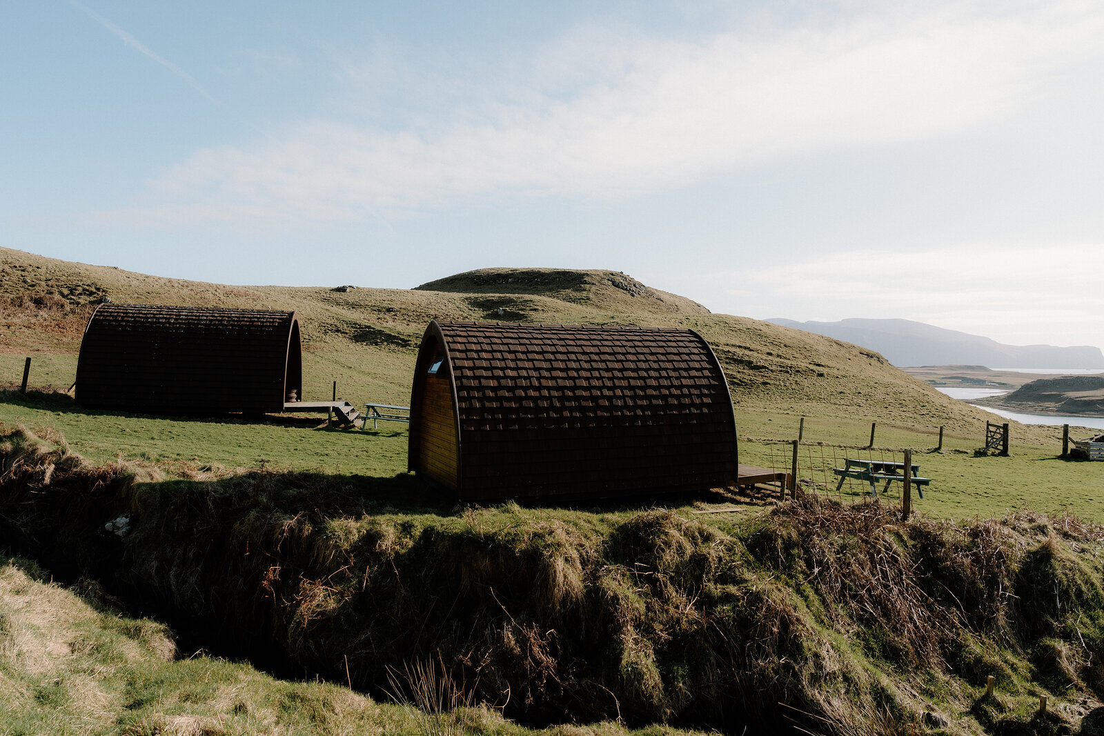 Two curved-roof camping pods sit on a grassy slope with picnic tables on the Isle of Canna.
