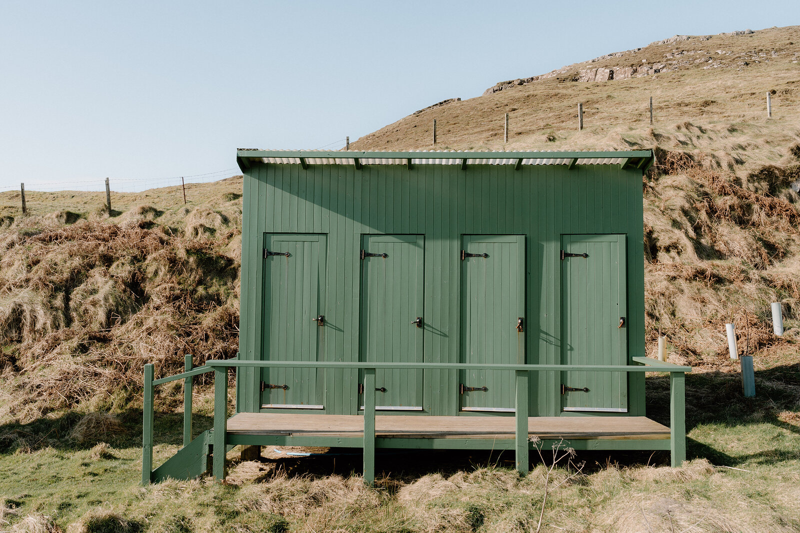 A green corrugated shower and toilet block sits on a grassy Canna hillside.
