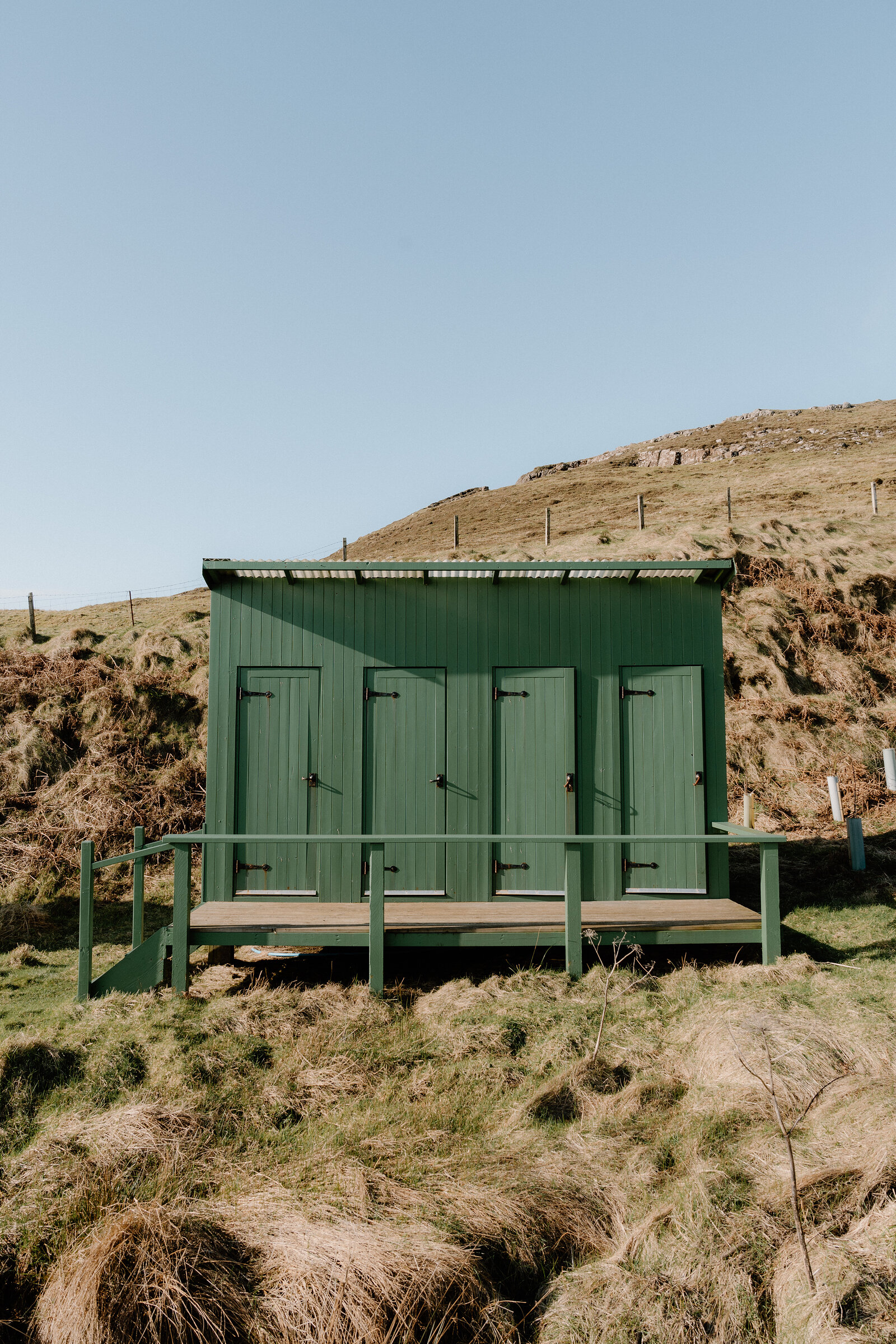 A green timber shower block stands on a boardwalk above a grassy slope on the Isle of Canna.