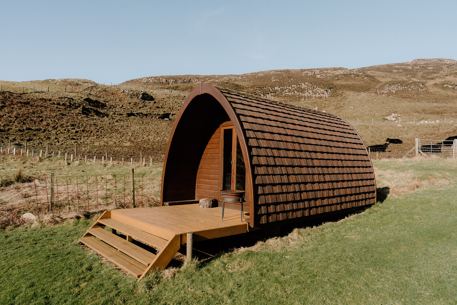 A dark timber camping pod with a curved roof sits on a grassy hillside on the Isle of Canna.