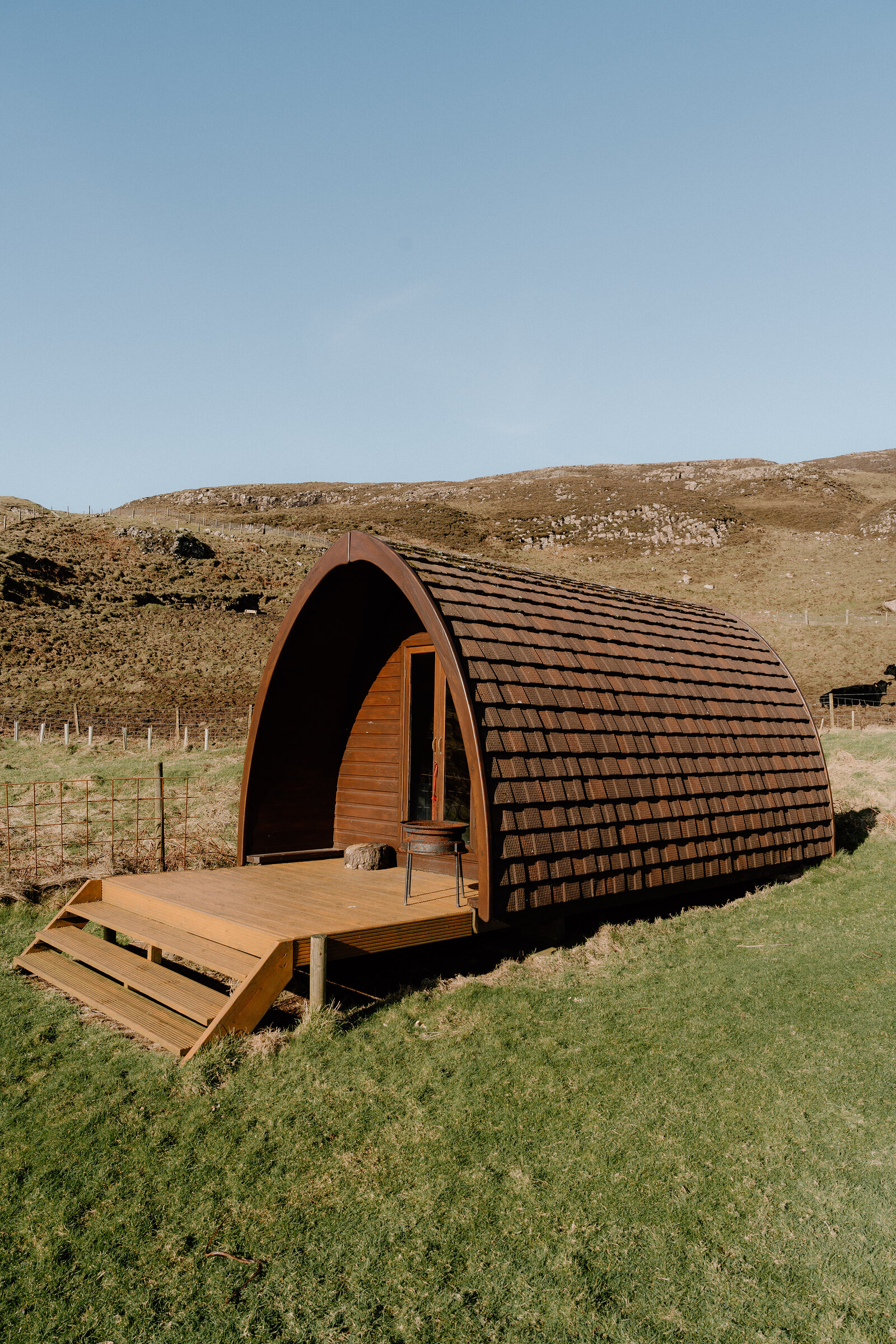 A curved-roof camping pod sits on open grass beneath a rocky hillside on the Isle of Canna.