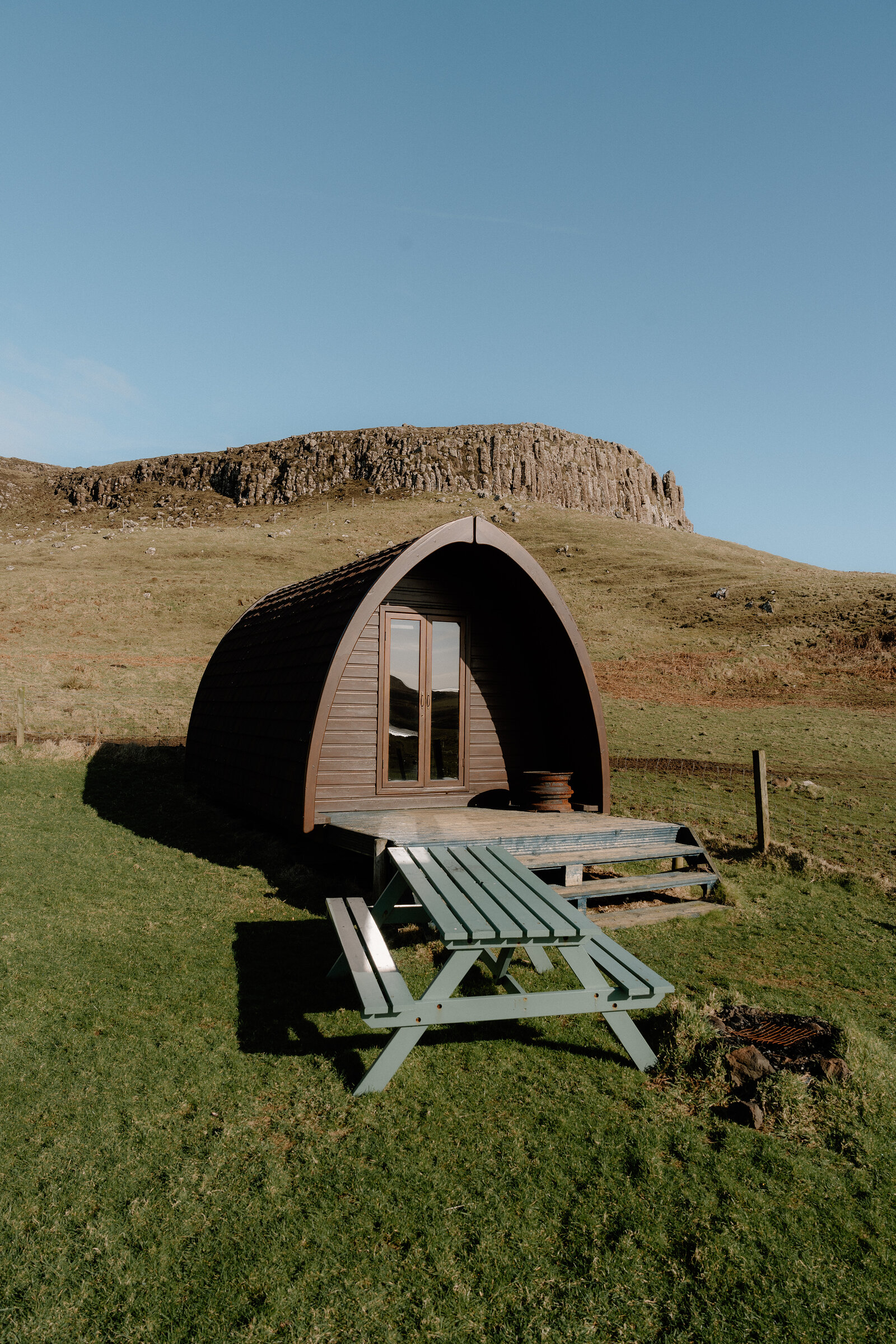 A dark timber camping pod sits below a rocky outcrop on the Isle of Canna.