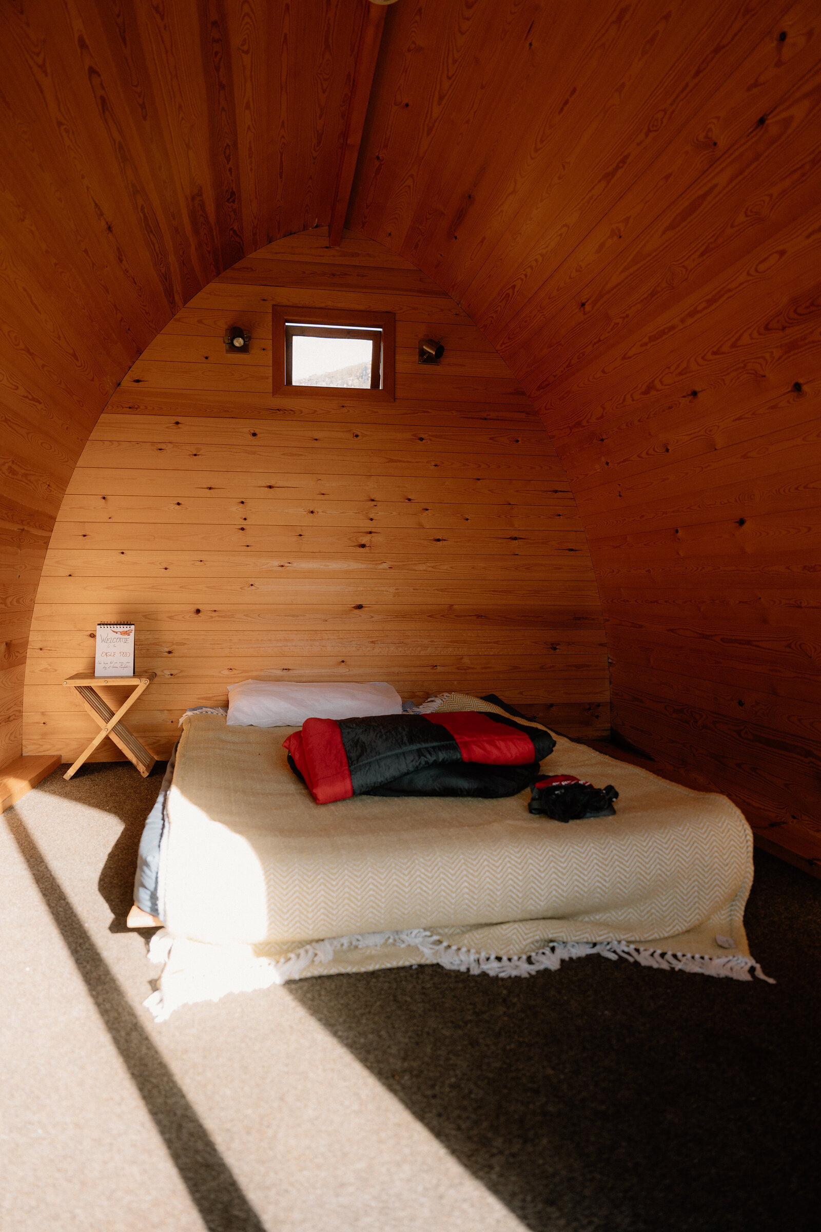 A tartan blanket lies folded on a bed inside a curved timber camping pod on the Isle of Canna.
