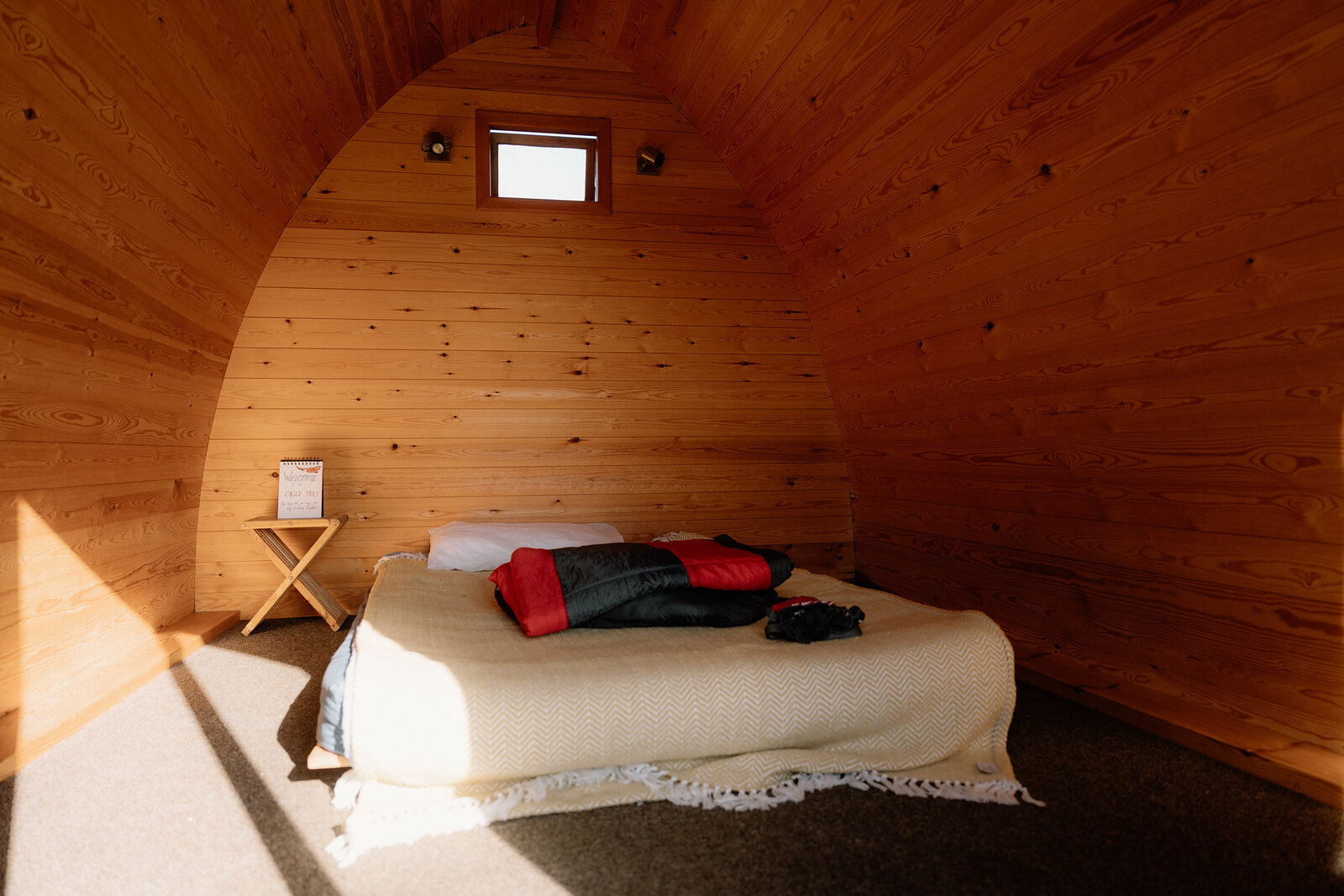 A bed with a tartan throw sits inside a curved timber camping pod on the Isle of Canna.