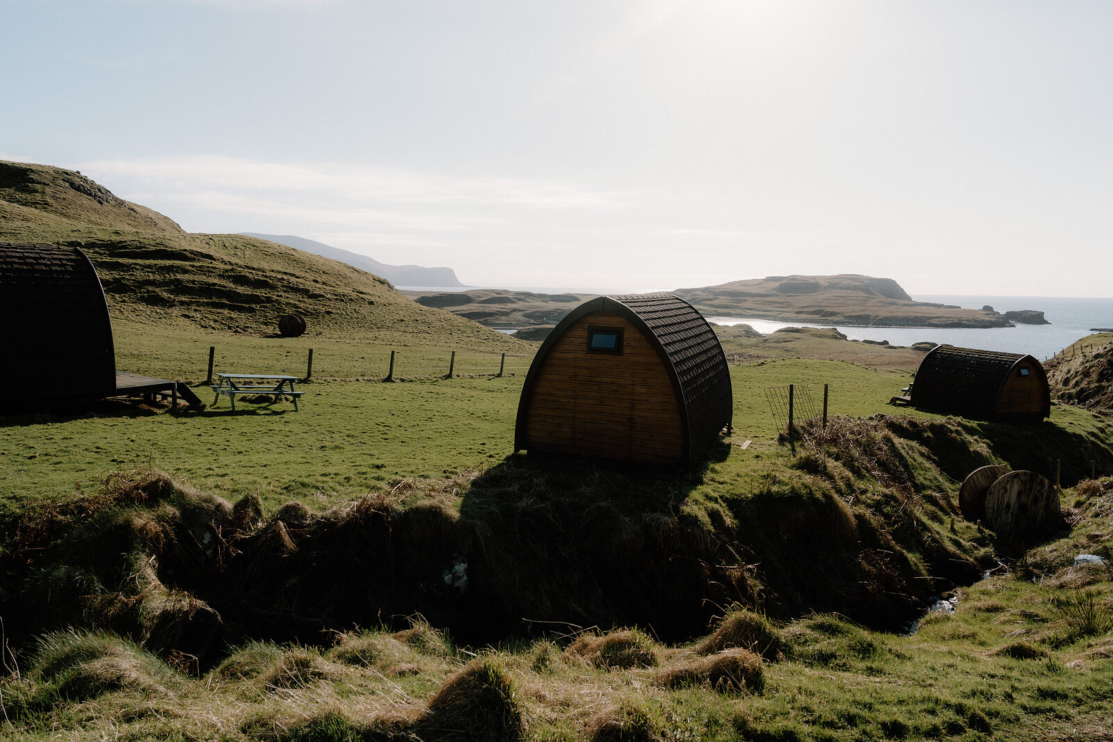 Camping pods sit on a grassy field overlooking the sea and distant islands on the Isle of Canna.